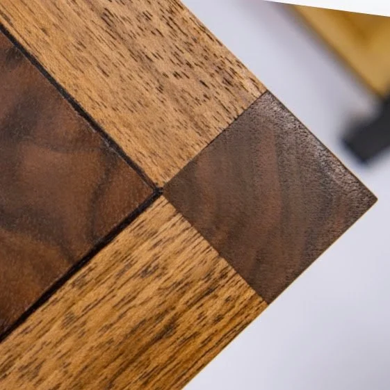 Close-up of a corner of a wooden table with a darker accent wood inlay.
