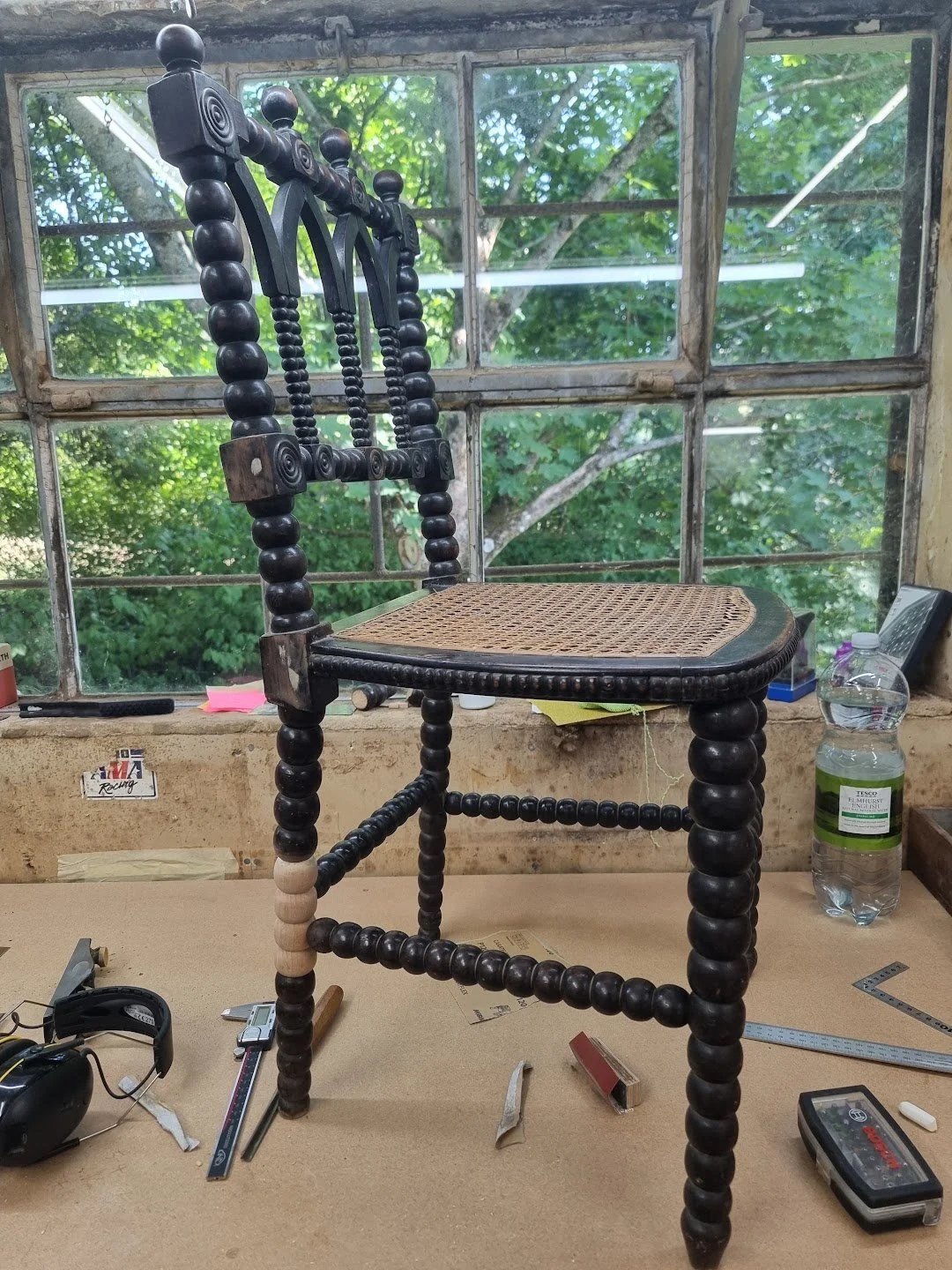 A vintage wooden bobbin chair with a woven cane seat, placed on a workbench during the process of restoration.