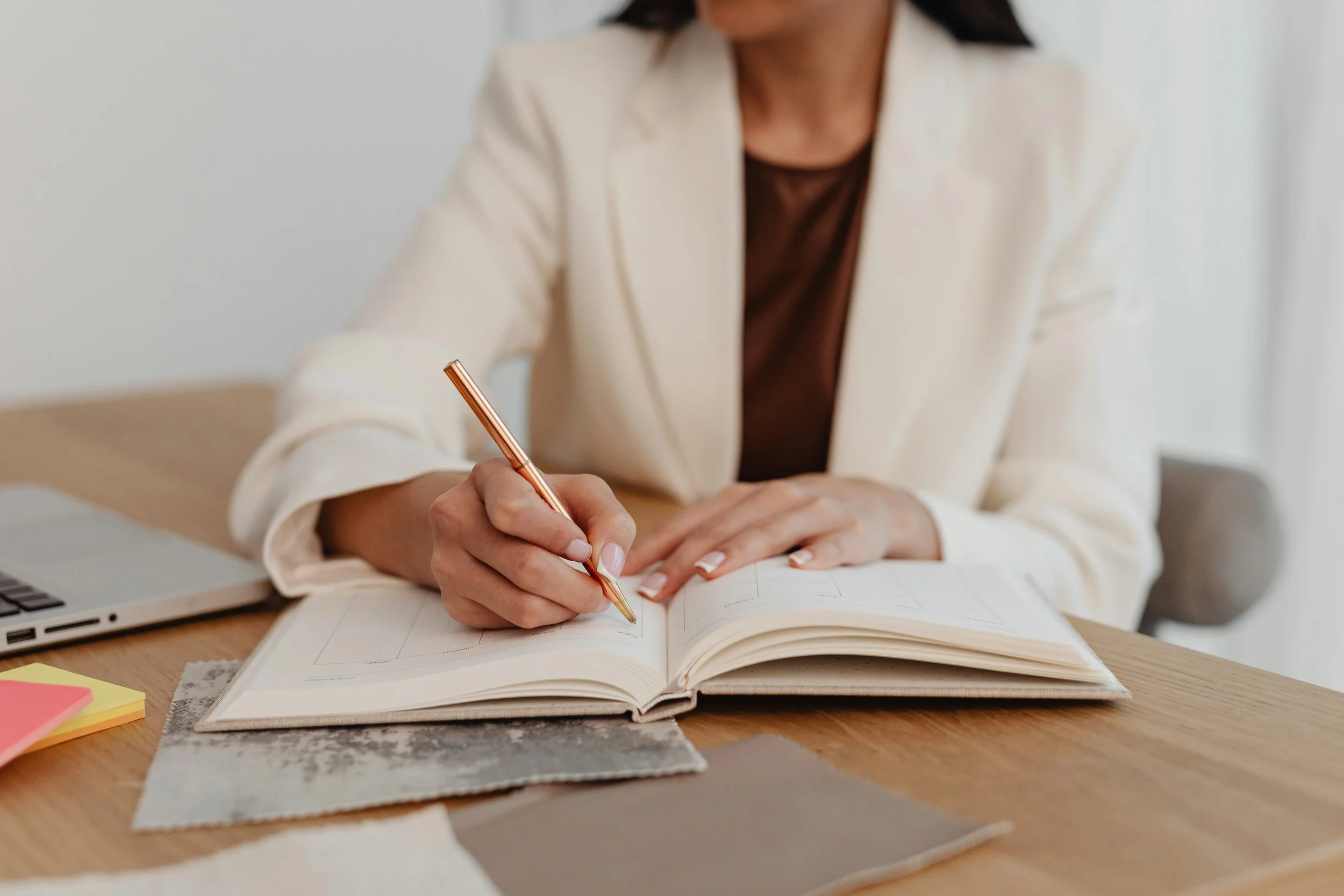 A woman in a cream blazer writes in a notebook