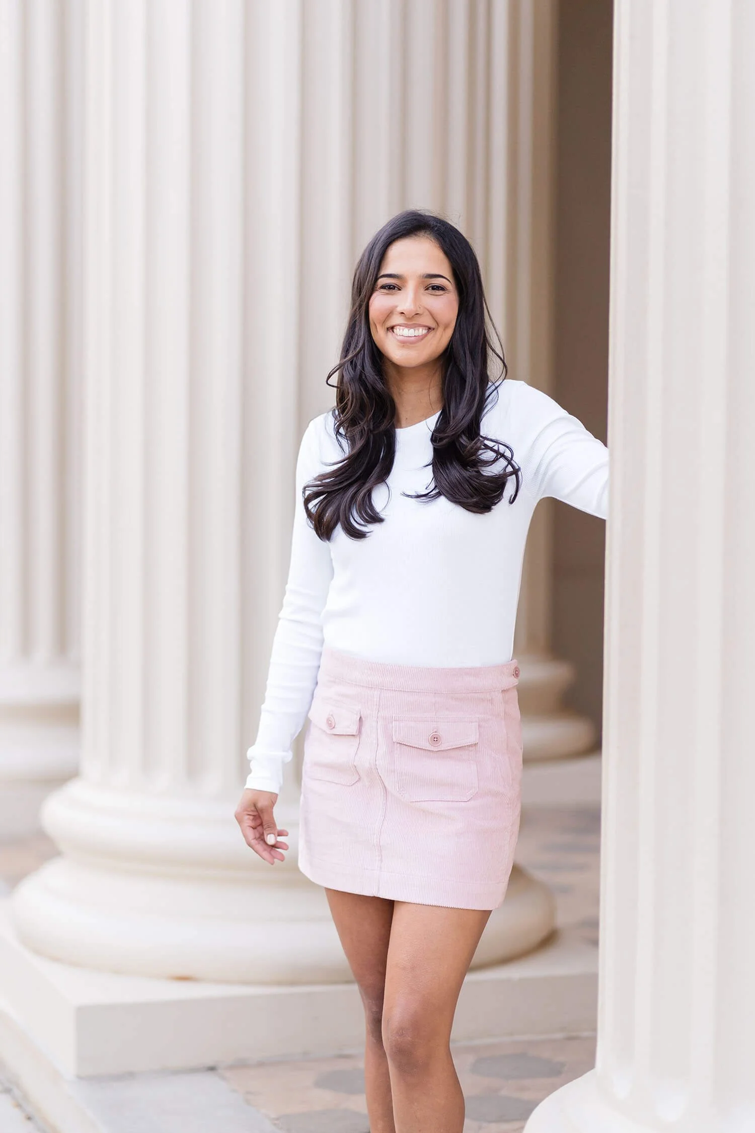 Lenet stands by an outdoor pillar in a white shirt and pink skirt
