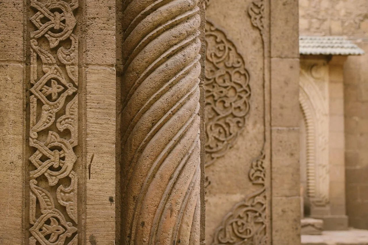 Close-up view of intricately carved stone architectural details on a historical building, featuring a twisted column in the center and decorative patterns on the sides.