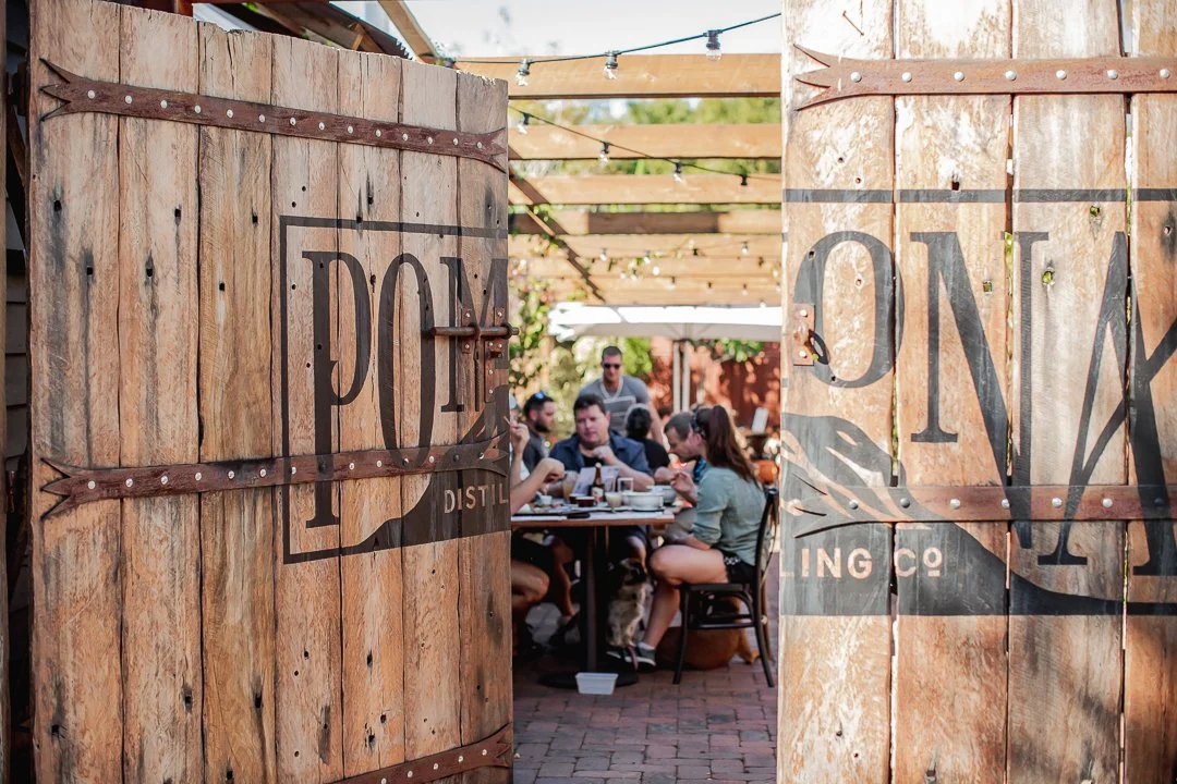 People dining outdoors at a rustic restaurant with wooden doors and string lights overhead.