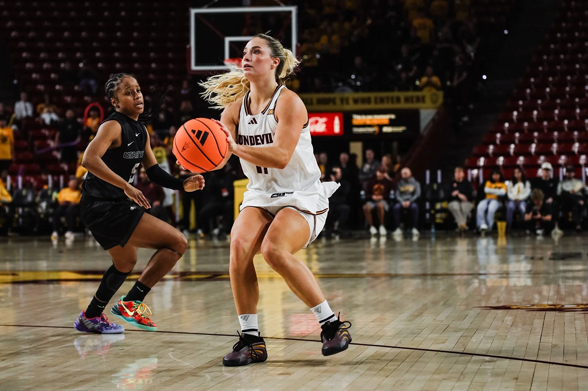 Two female basketball players in action on a basketball court, one in a white jersey and the other in a black jersey, with a basketball in hand, during a game.