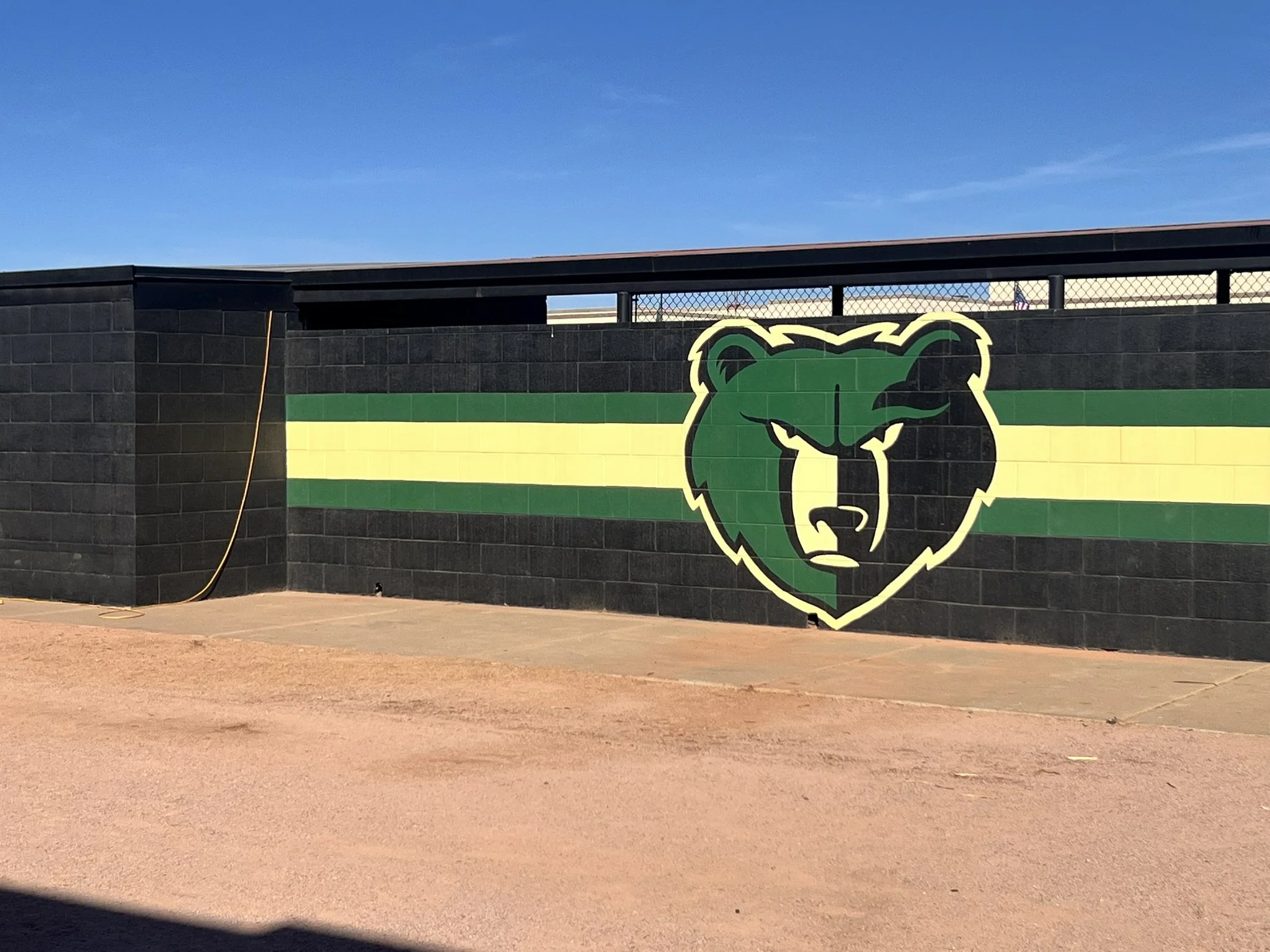Softball dug out with dirt in front of it and a bear painted on the wall