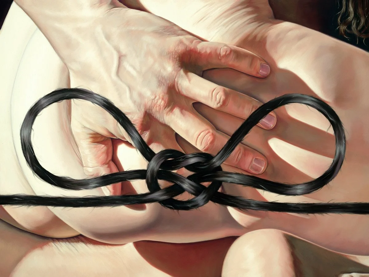A close-up of a hand with fingers spread, resting on a skin-toned surface, with black hair strands tied in a loop on top of the hand.