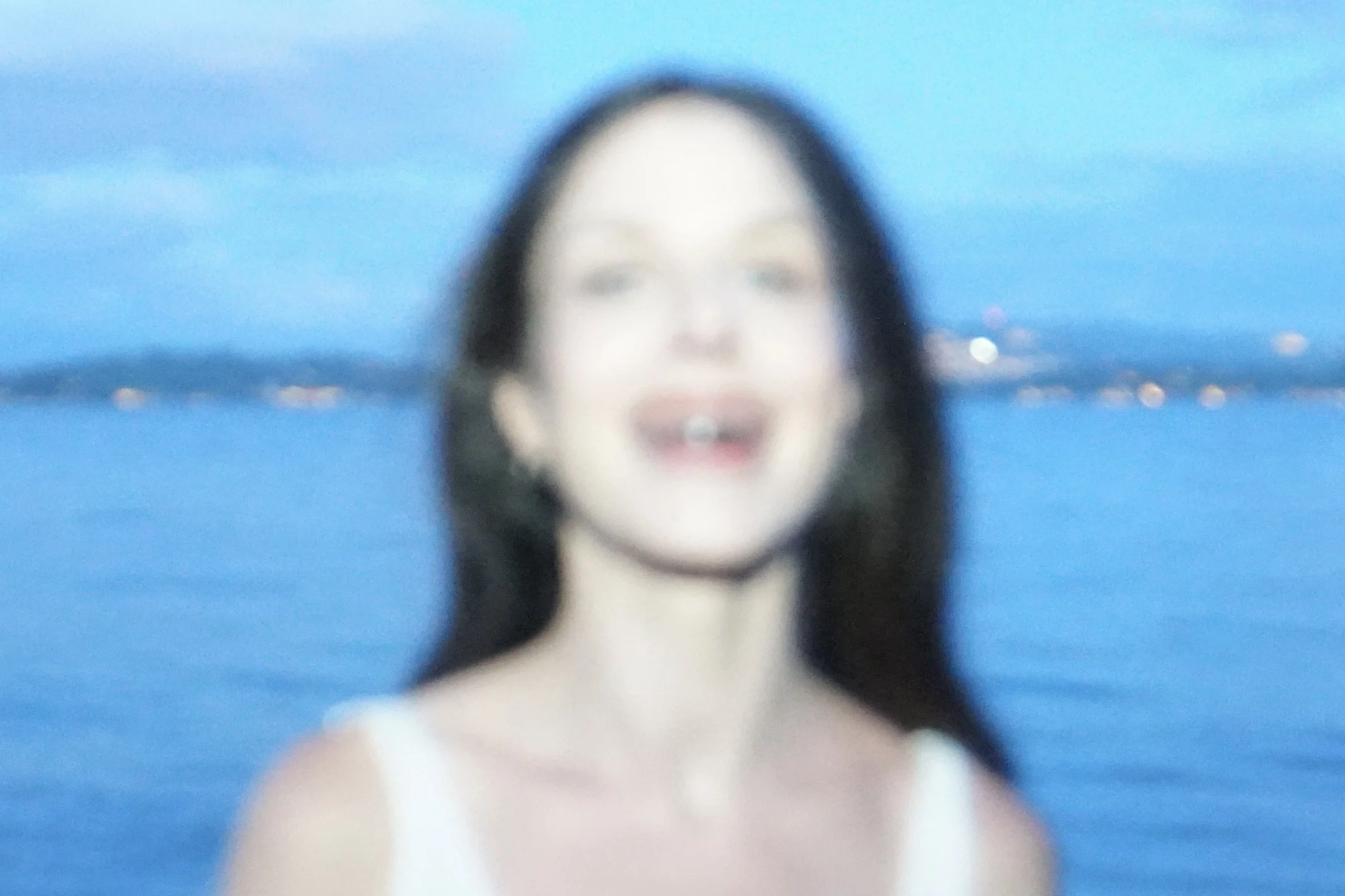 Blurry close-up image of a woman with dark hair and light skin, against a blue background.