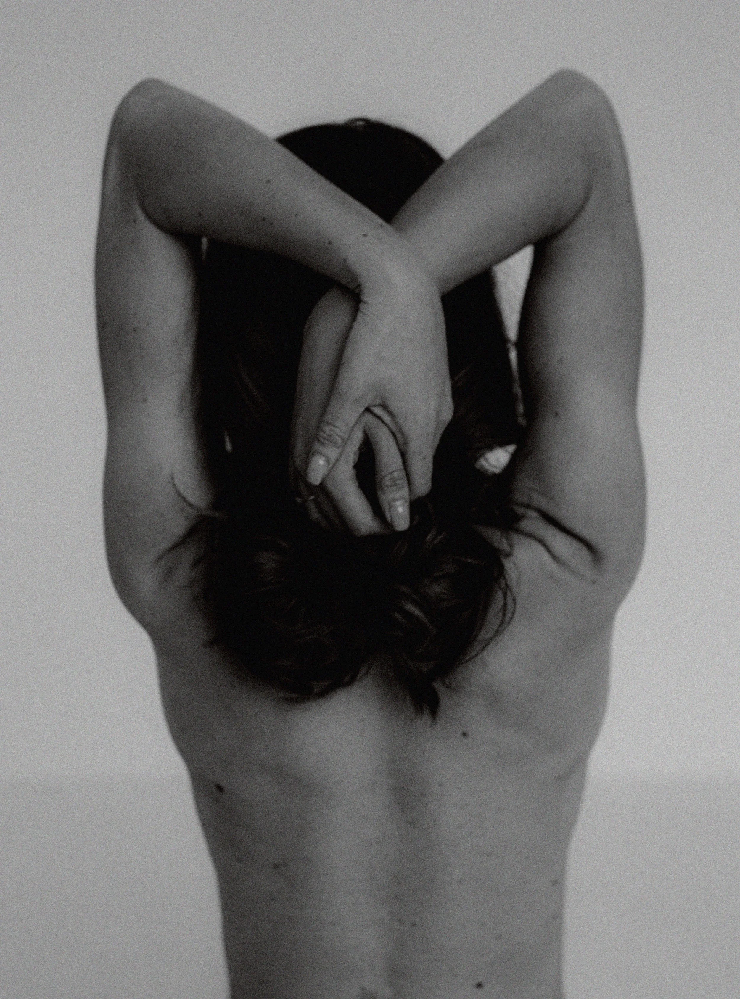 A person with dark hair is seen from behind, with arms raised and hands intertwined behind their head, creating a circular shape.