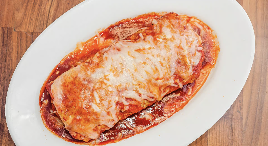 A plate of a Mexican wet burrito topped with melted cheese and sauce, served just for you.