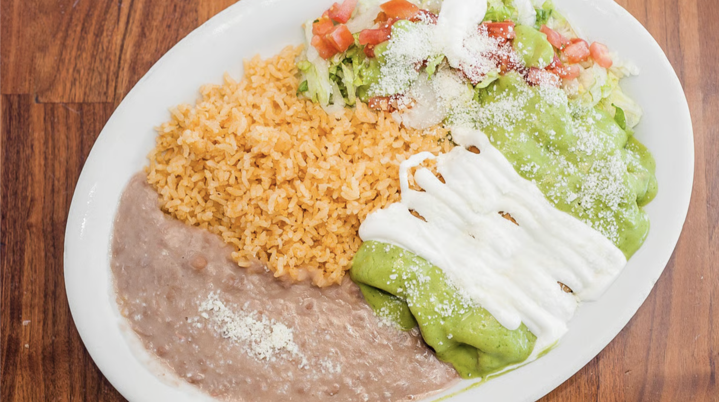 Platter of a Mexican flautas with rice, refried beans, and the flautas with green sauce, sour cream, shredded cheese, lettuce, and tomatoes.