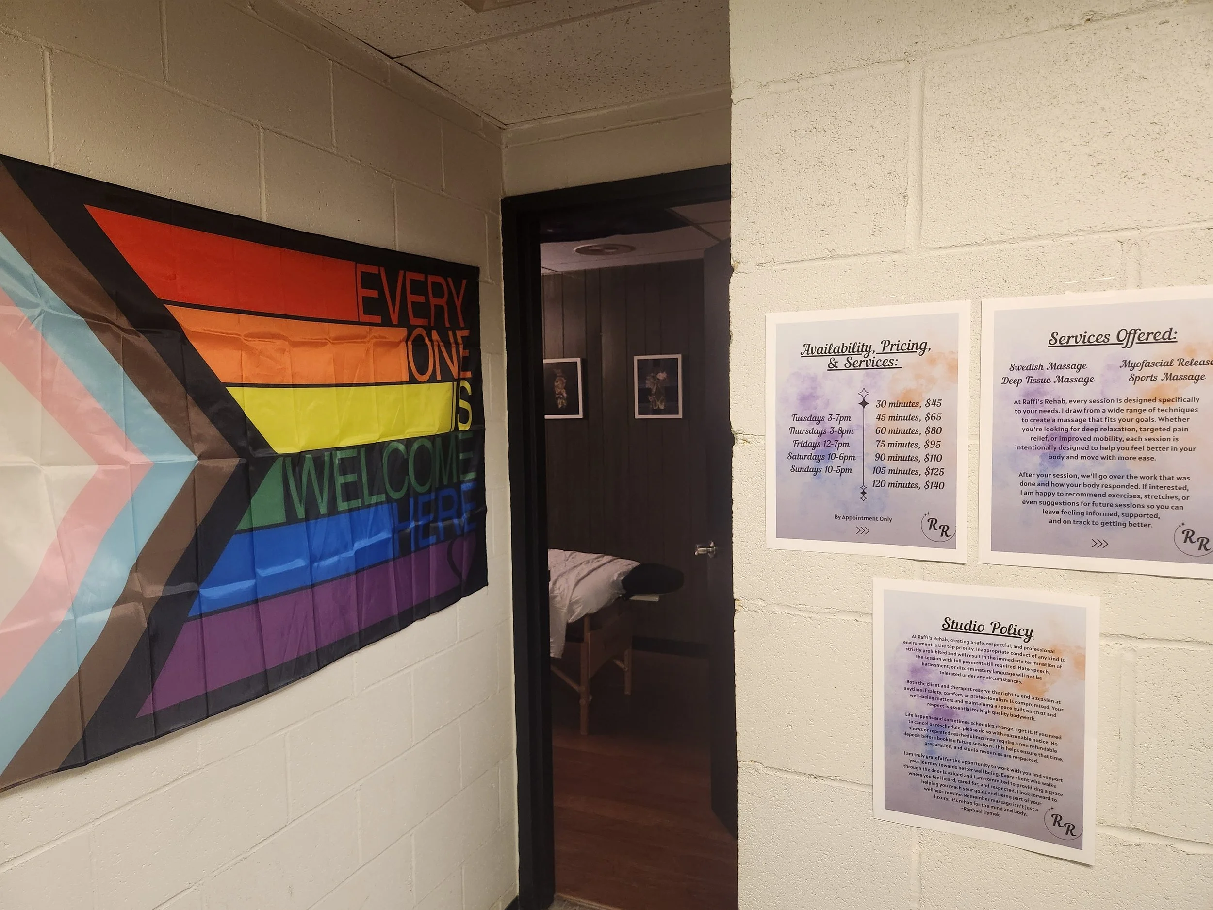 Colorful pride flag with the words "Everyone is Welcome Here" hung on a white wall.