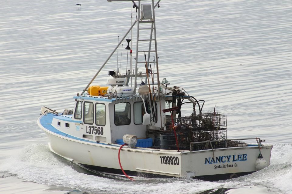 A fishing boat named Nancy Lee sailing on calm water with fishing traps and equipment onboard.