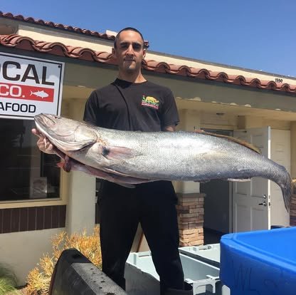 Man holding a large fish in front of a restaurant.