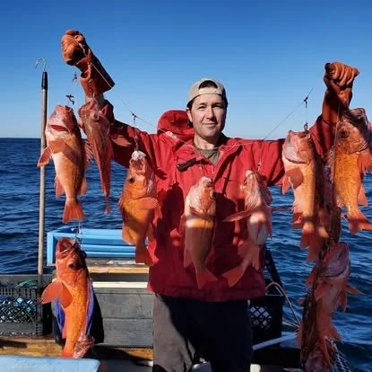 Man holding a fishing line with multiple red sea fish caught, standing on a boat in the ocean during daytime.