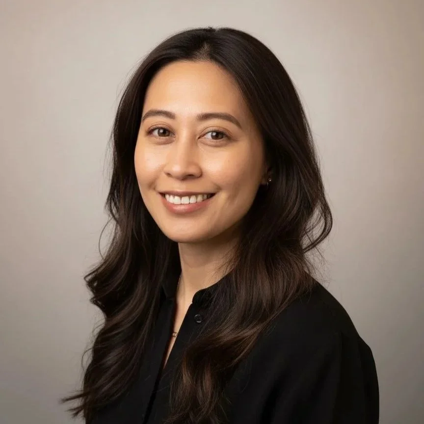 A young woman with long dark hair smiling, wearing a black shirt, against a plain grey background.