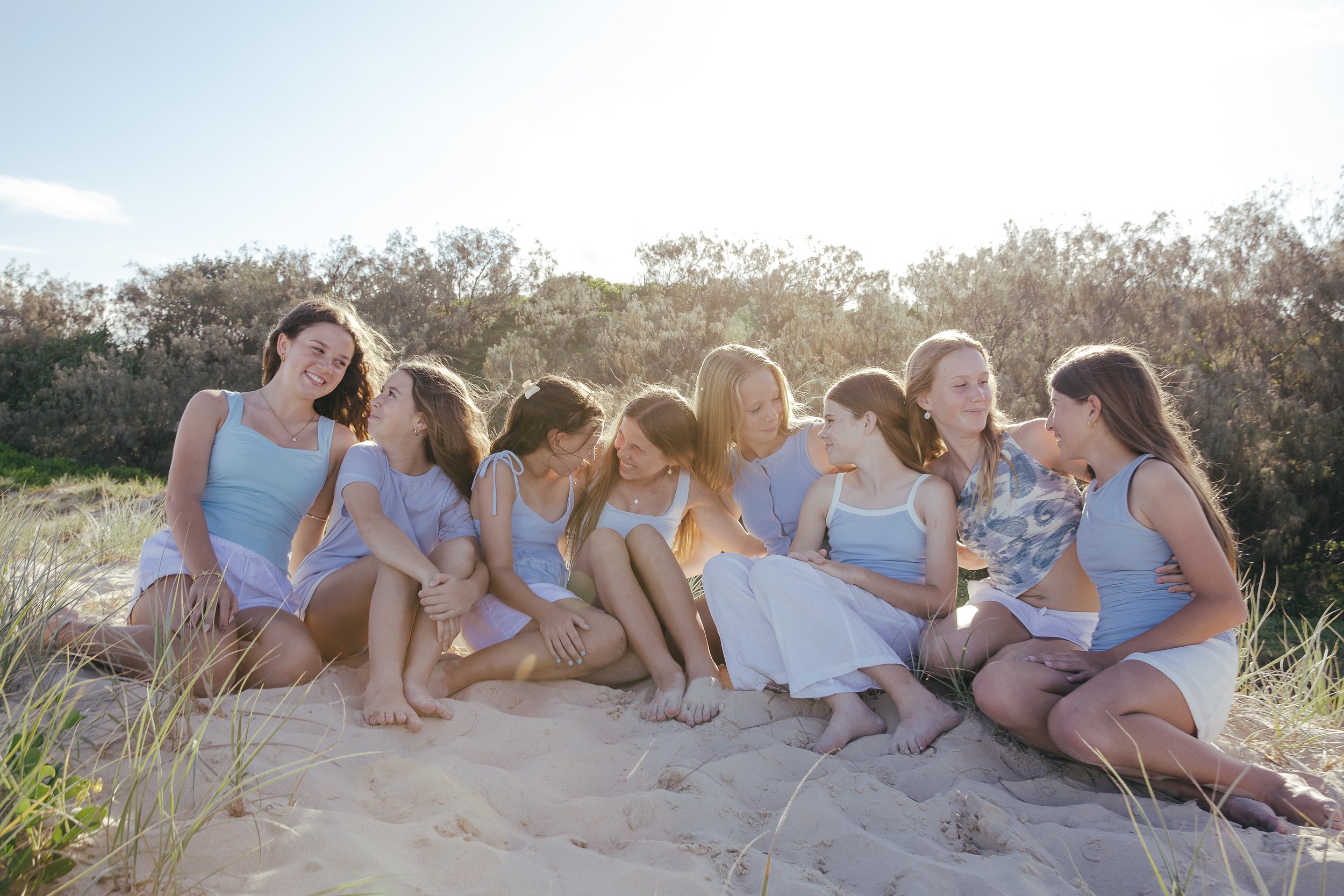 A group of young women sitting on the sandy beach, smiling and enjoying each other's company on a sunny day.