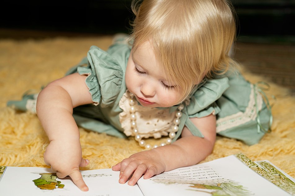 toddler girl reading a book on yellow rug.jpg