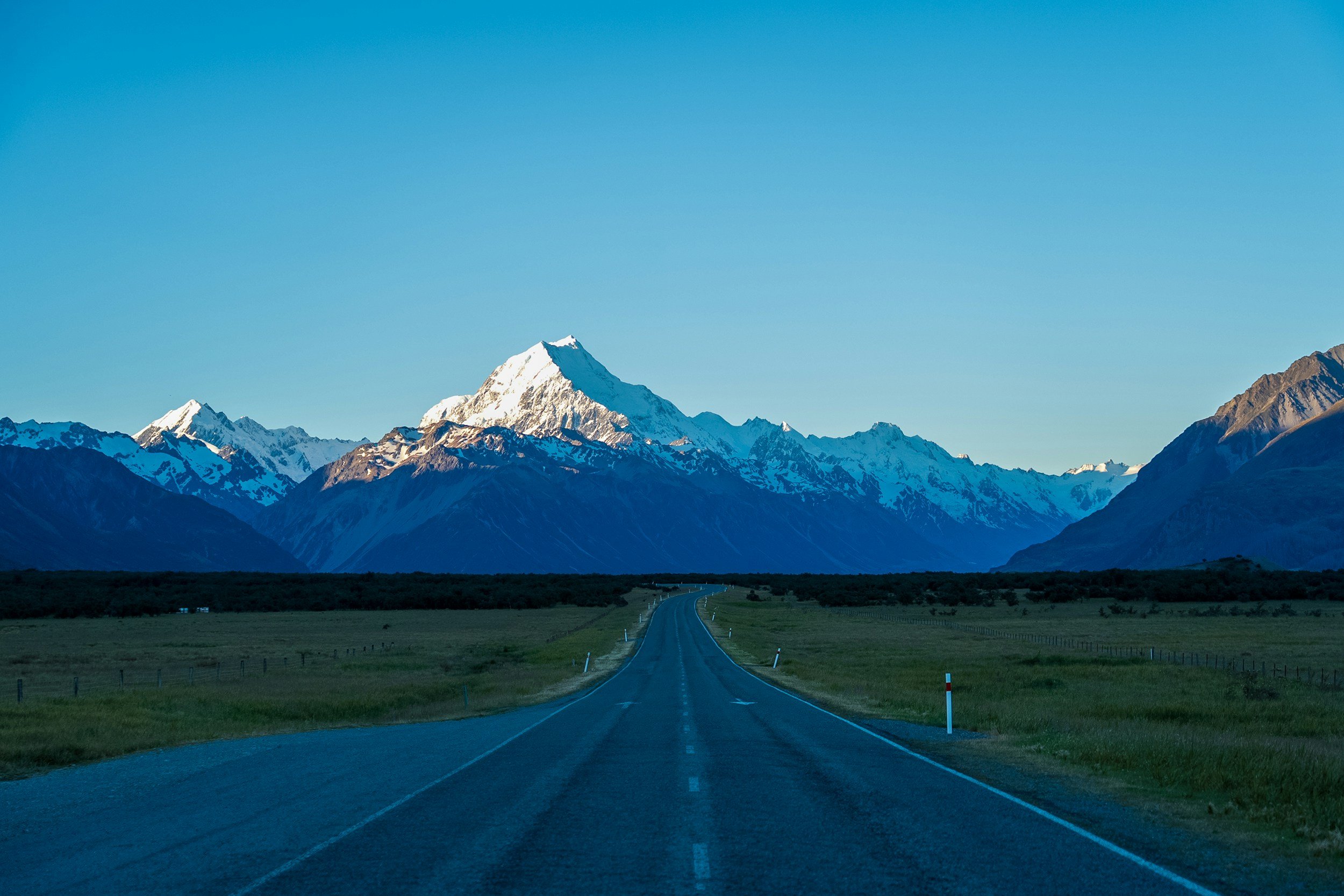 An open road leading towards snow-capped mountains under a clear blue sky.