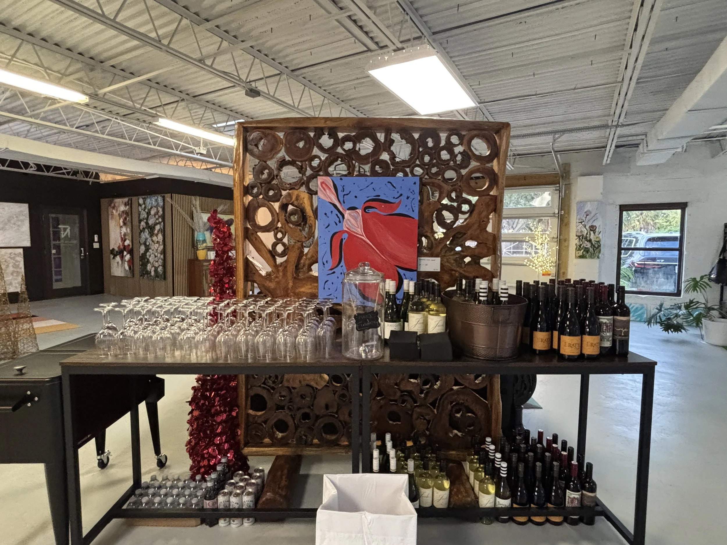 Display of wine bottles, glasses, and wine accessories on a table in an art gallery.