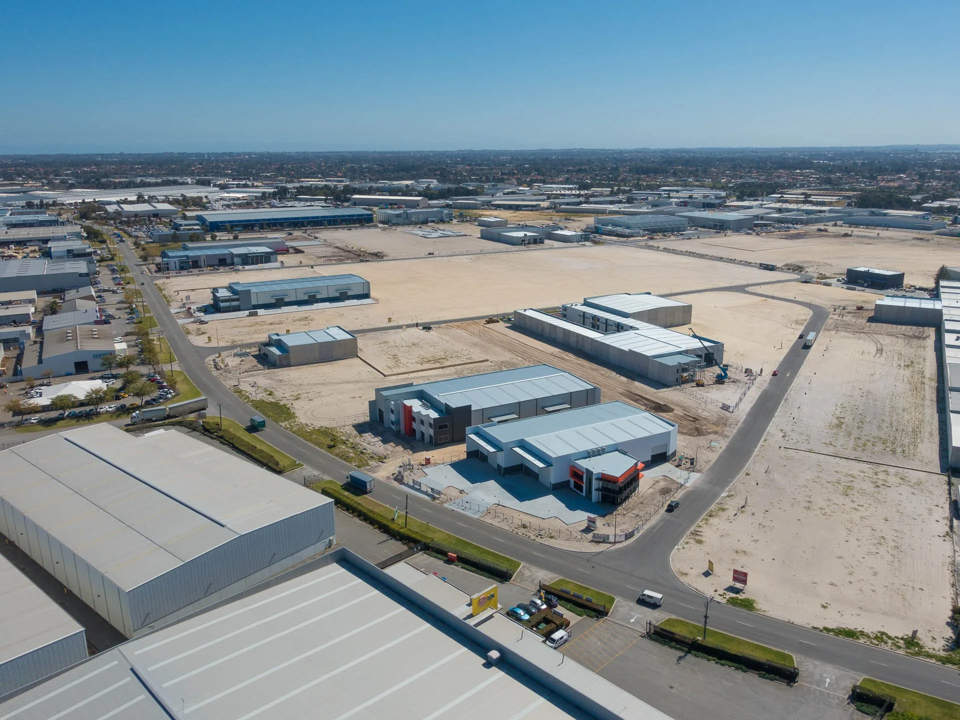 An aerial view of a commercial area with numerous unfinished buildings, construction sites, and a network of roads, under a clear blue sky.