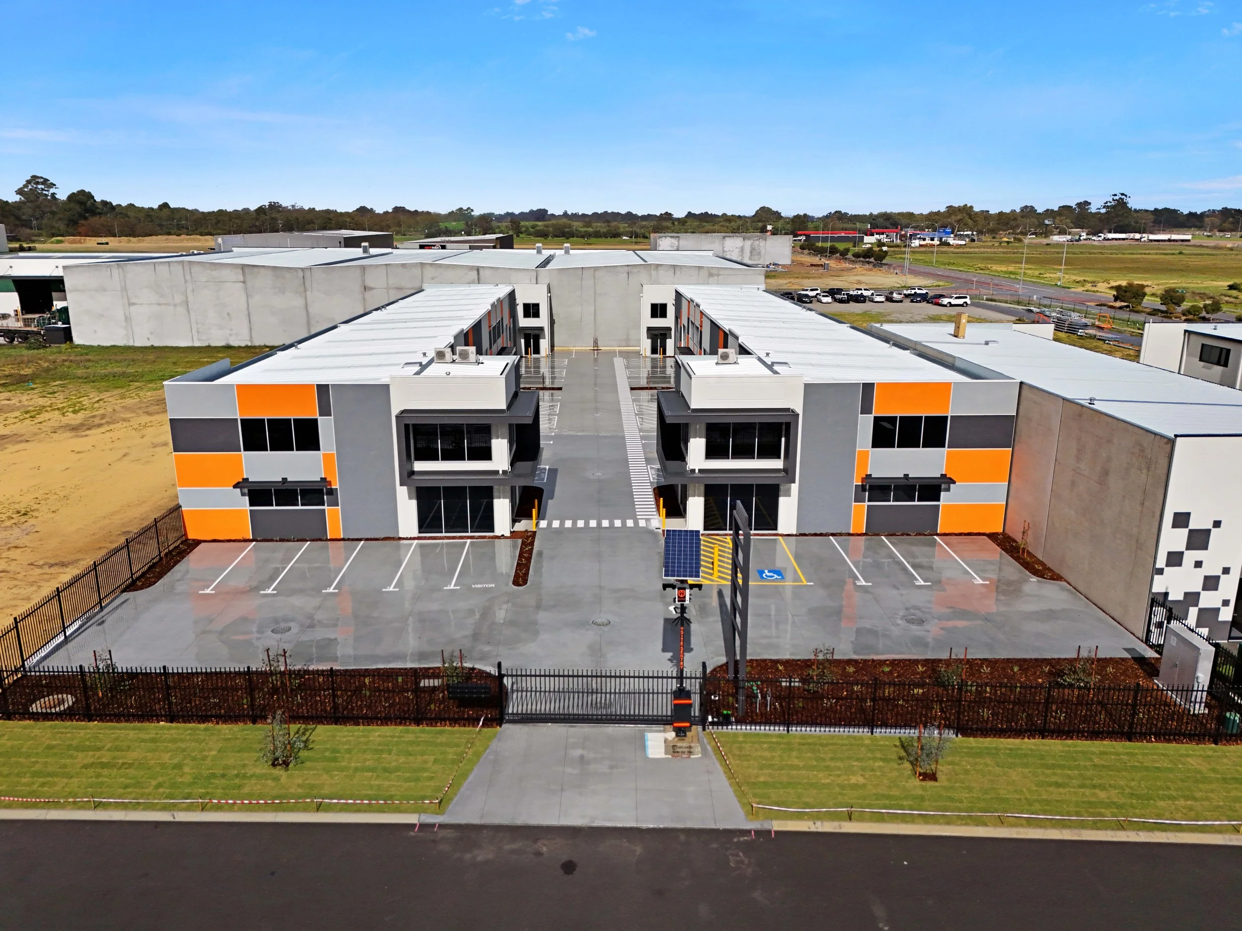A newly constructed modern commercial building with parking lot and landscaping, featuring gray, orange, and black exterior design.