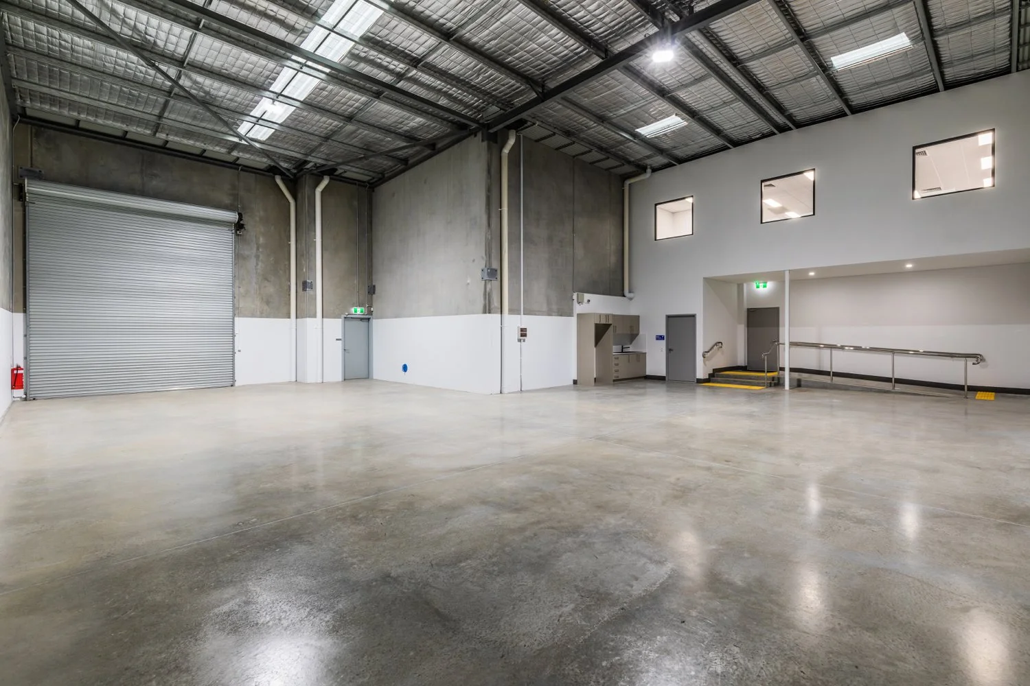 Empty industrial warehouse with polished concrete floor, metal roof, and white walls.