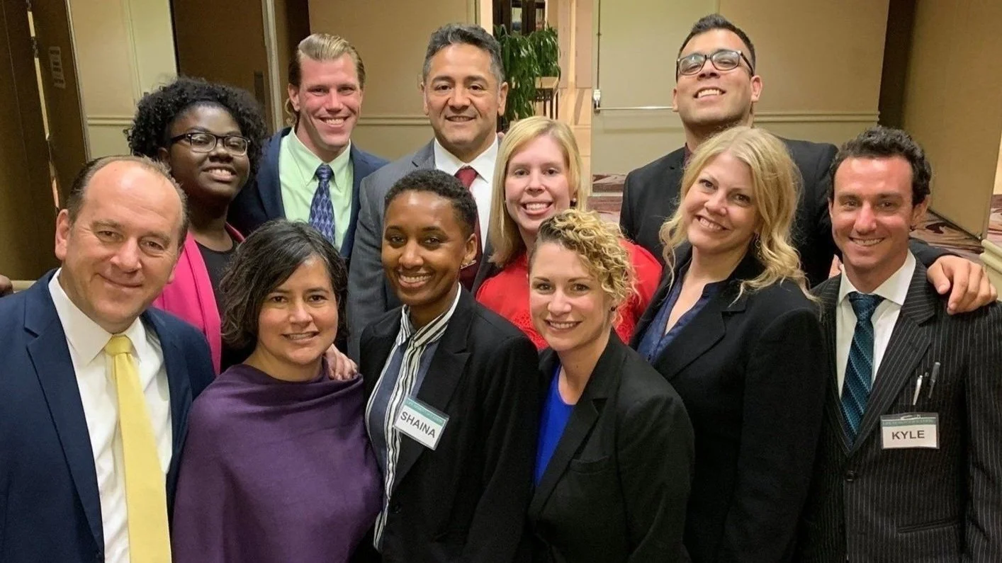 Group of twelve diverse professionally dressed people smiling at a conference or event in an indoor venue.