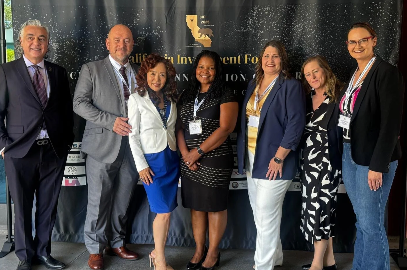 Group of seven professionals at the California Investment Forum, standing in front of a dark backdrop with event branding.