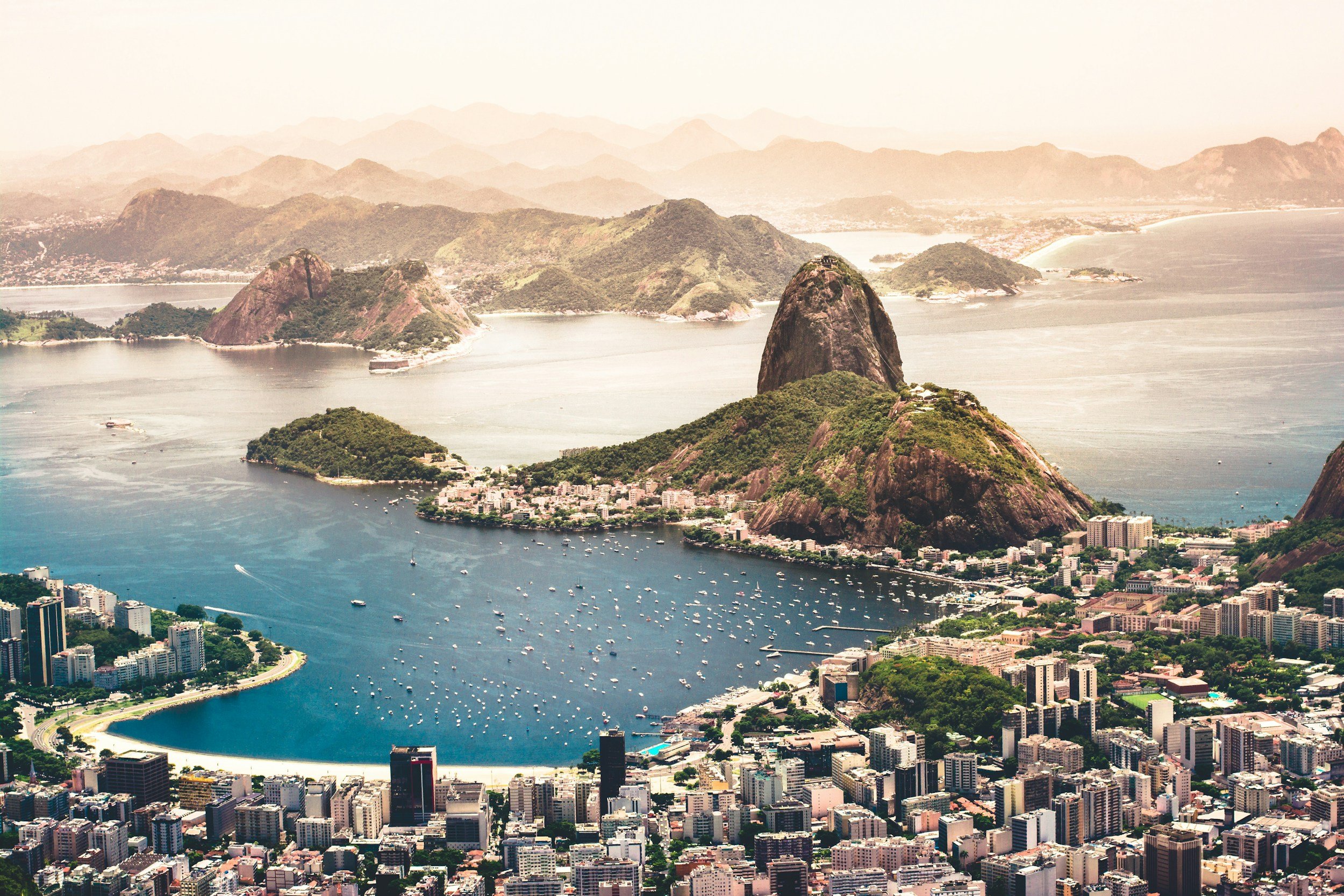 An aerial view of downtown Rio de Janeiro with Sugarloaf Mountain, the city skyline, and Guanabara Bay.