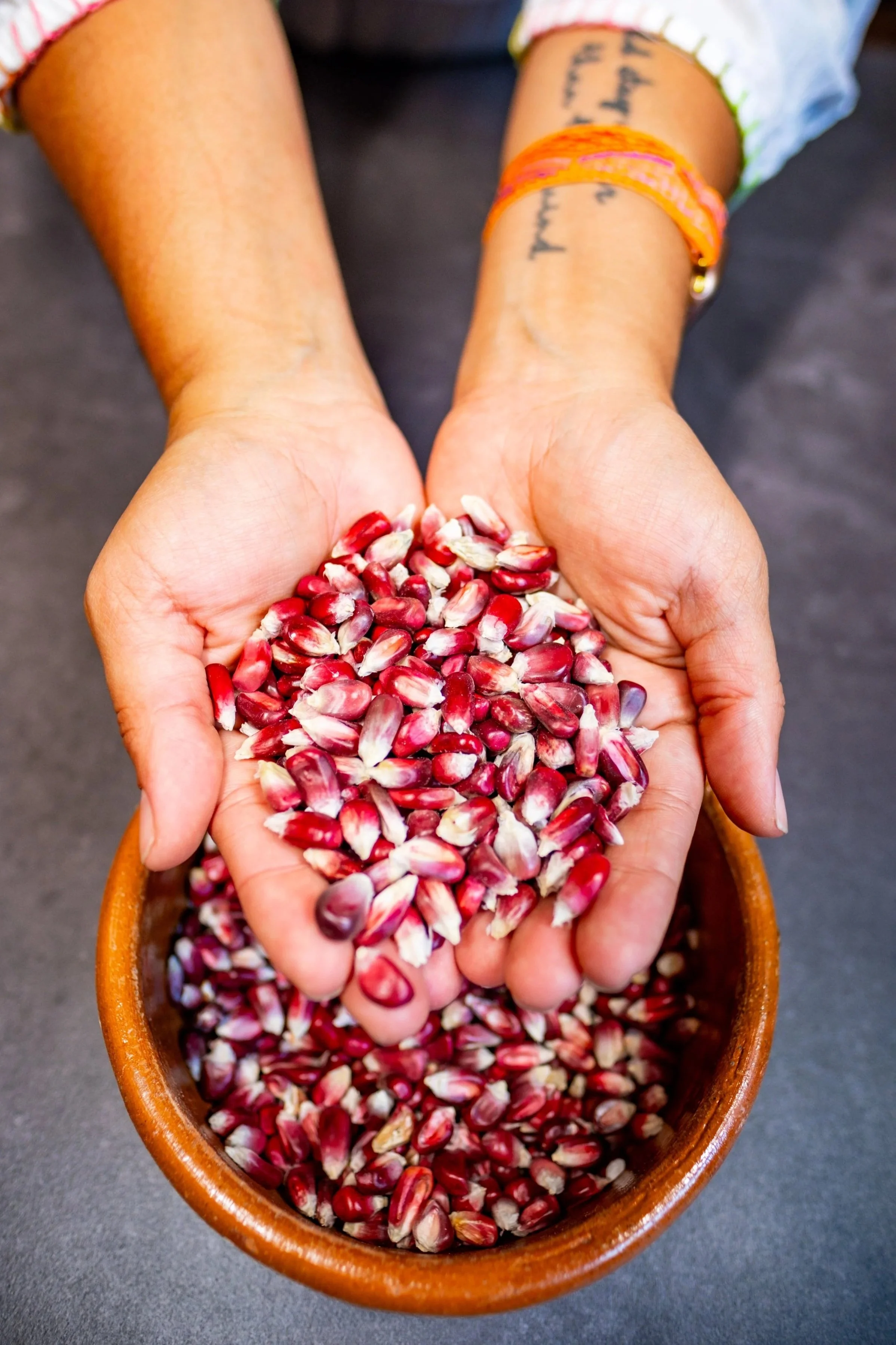 Hands holding pomegranate seeds over a wooden bowl.