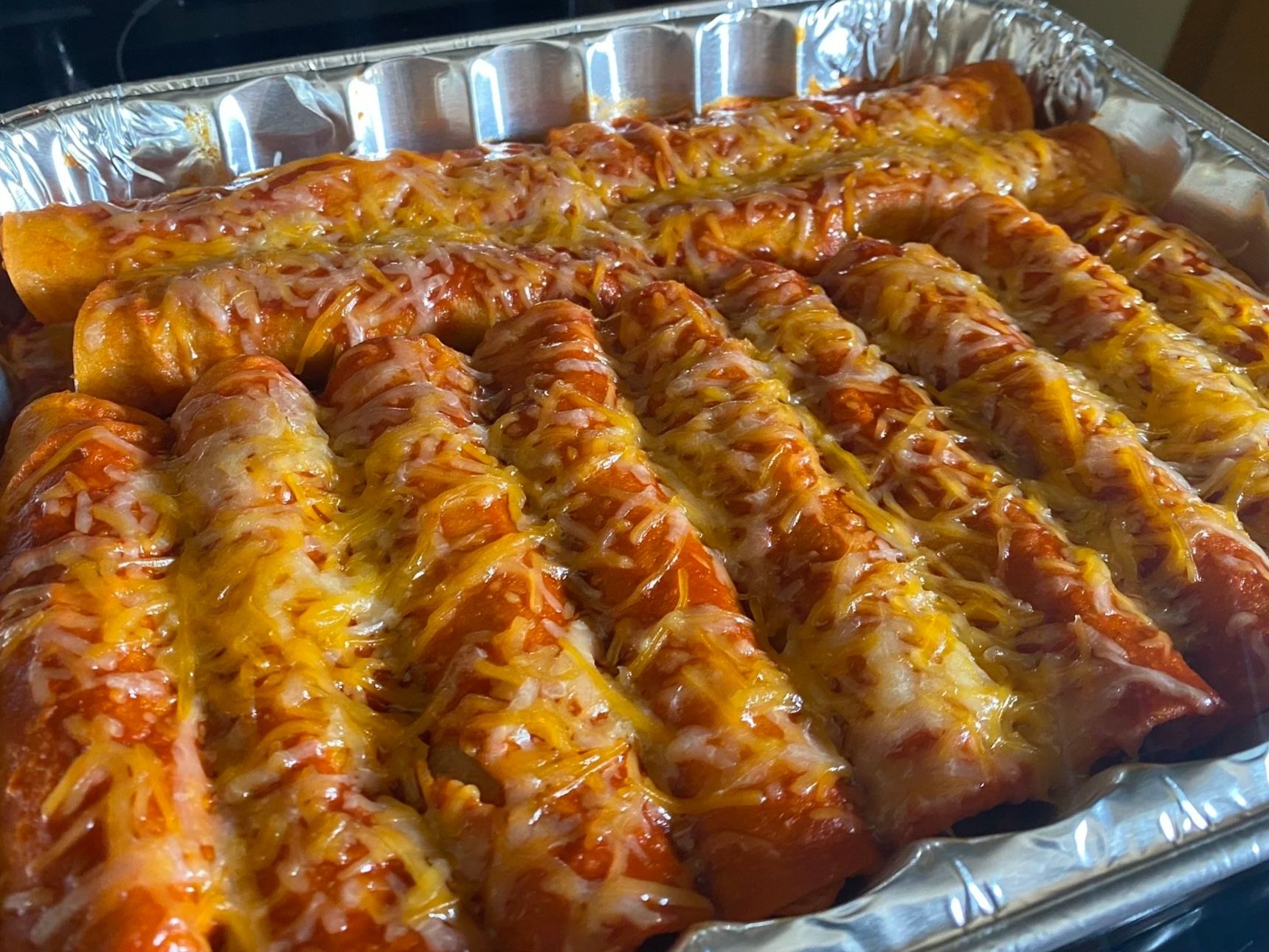 Tray of cheesy beef and potato enchiladas with melted cheese on top.