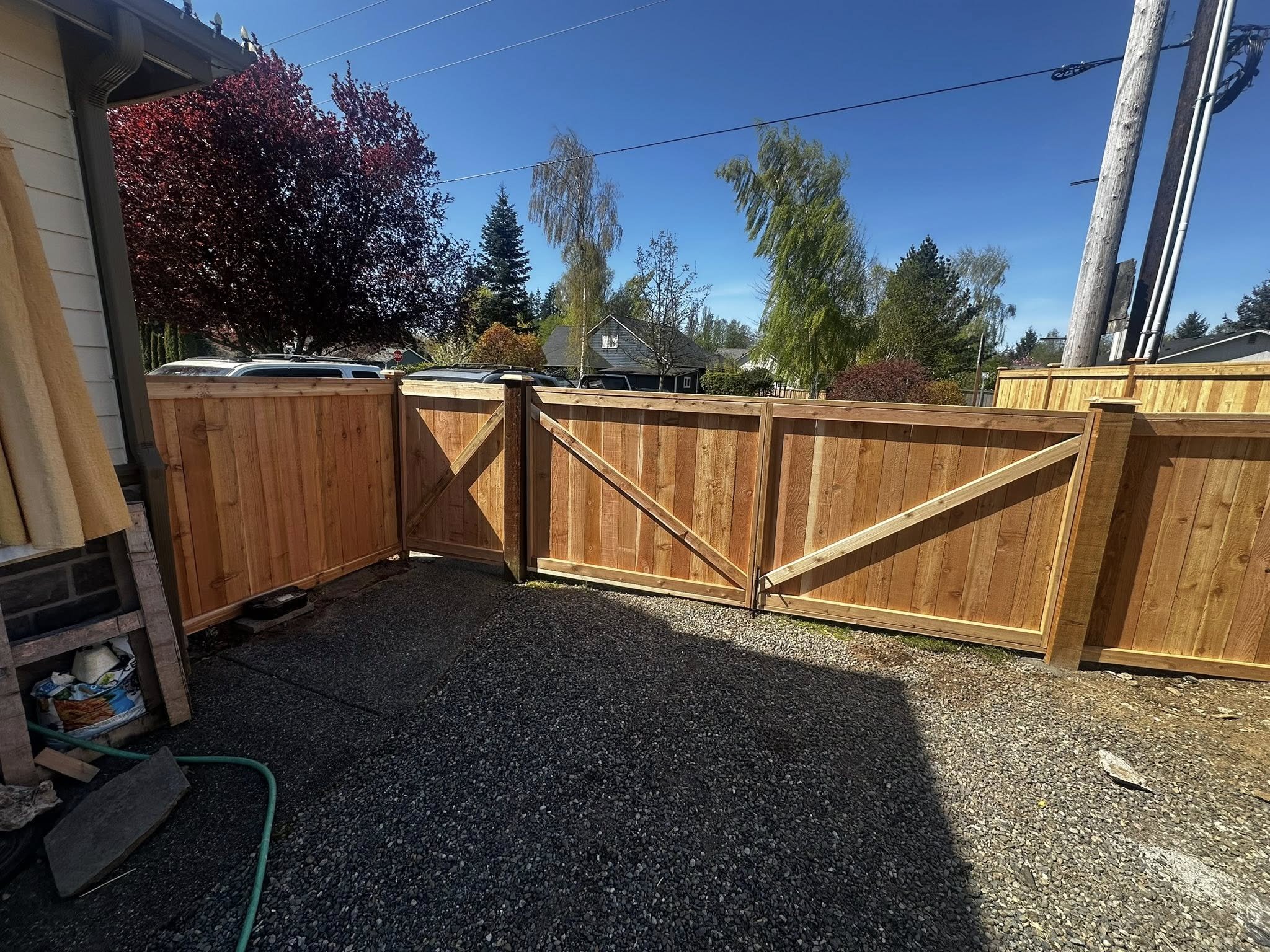 A backyard with a freshly installed wooden privacy fence, gravel ground, and trees under a clear blue sky.