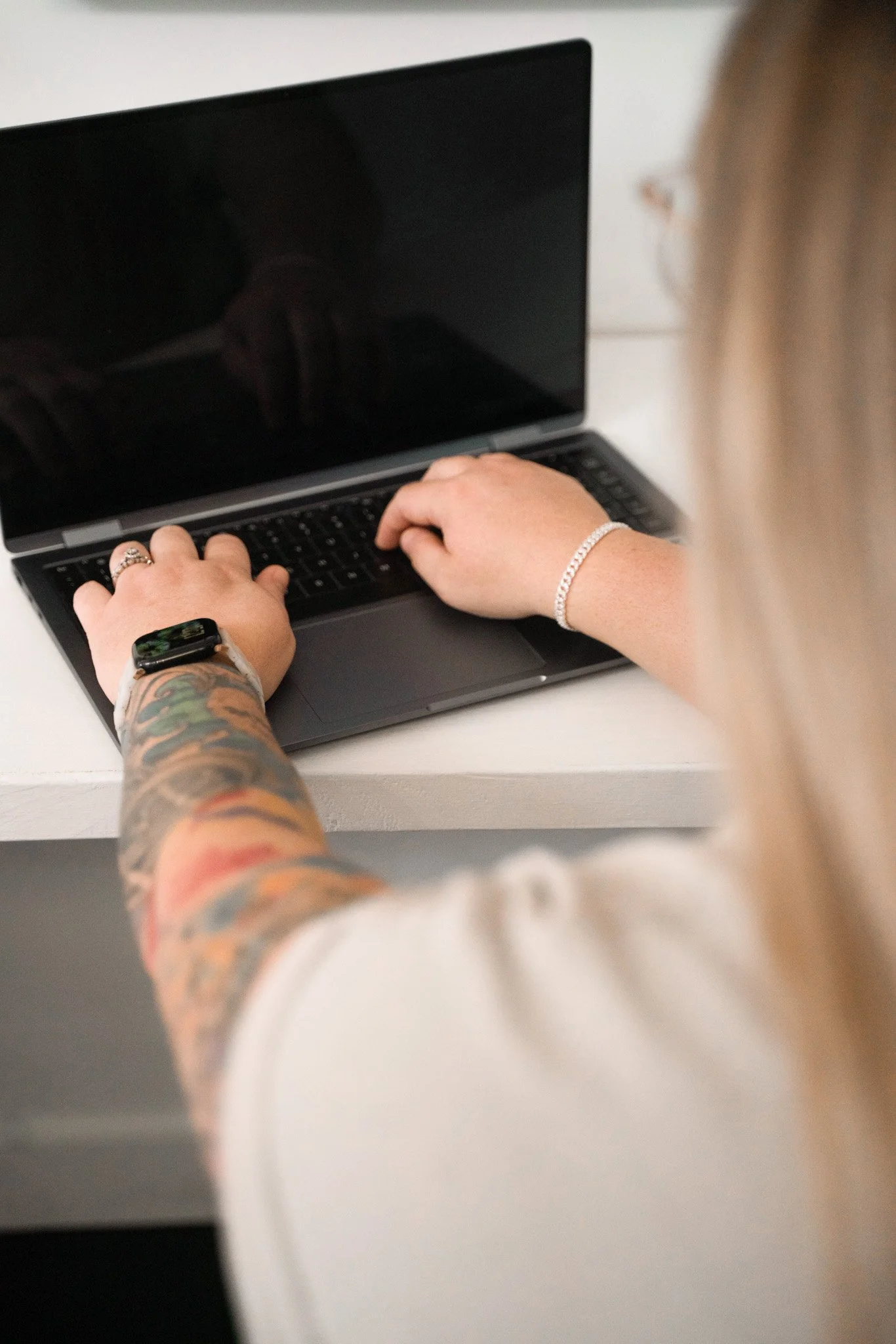 Ansley Warner wearing a watch and a bracelet is typing on a laptop with a black screen.