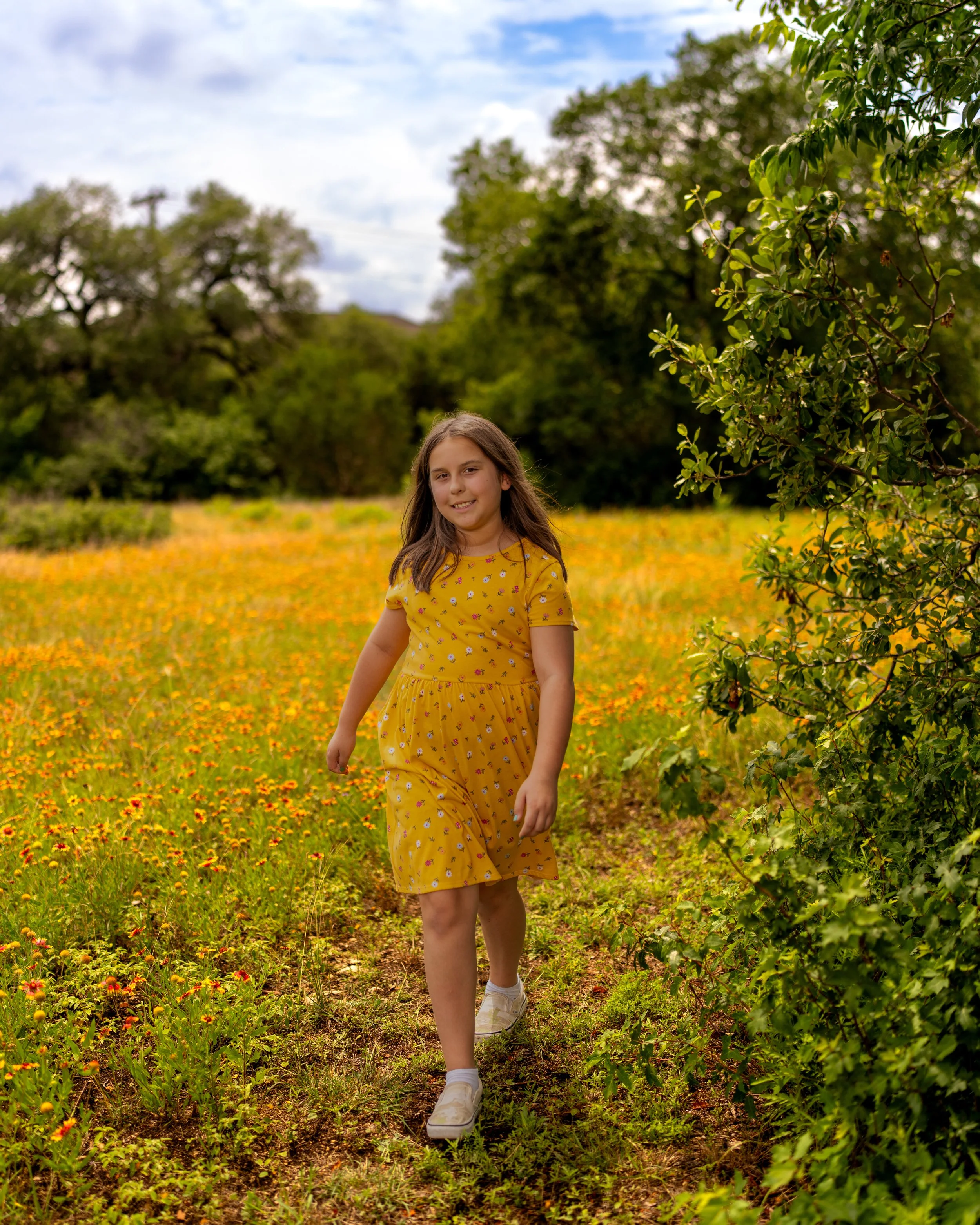 Girl walking through field of yellow and orange wildflowers. Photo taken in Austin Texas by an Austin Texas photographer.