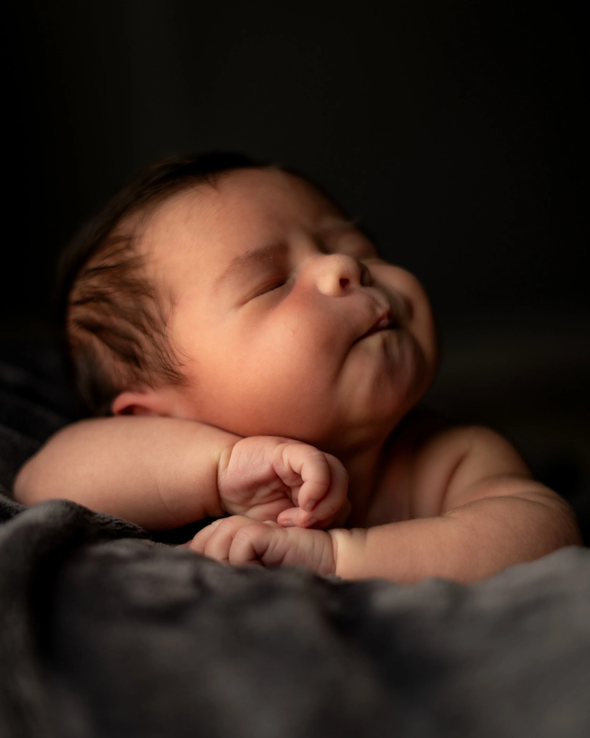 Portrait of a sleepy baby girl stretching while laying belly down on a plush grey blanket. Photo taken in Austin Texas by an Autin Texas  photographer.