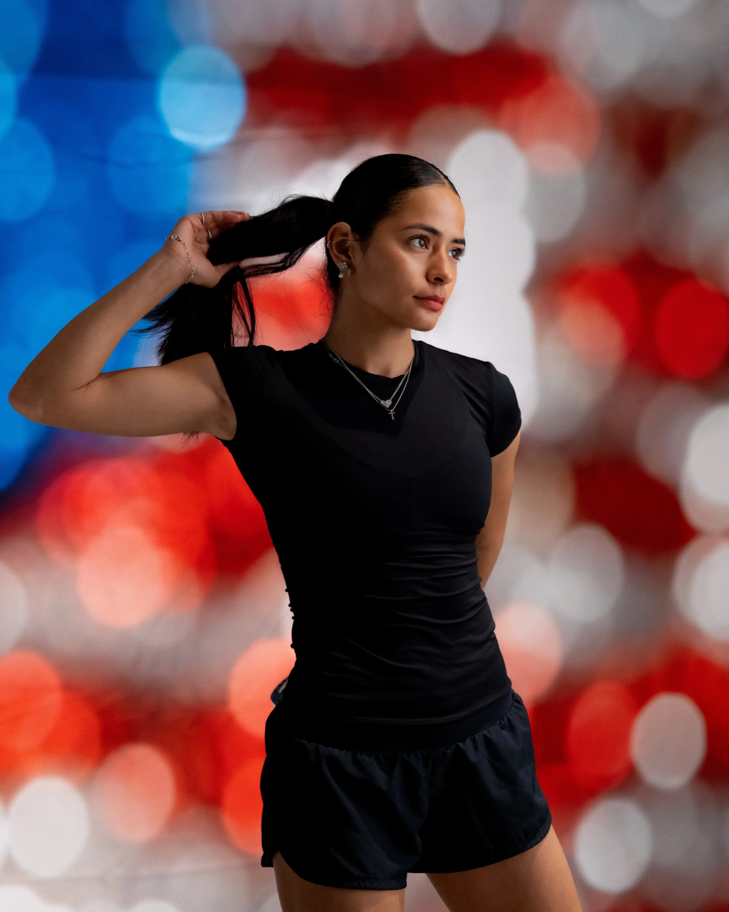 Sports portrait of a fit girl playing with hair in front of American Flag. Portrait taken by an Austin Texas photographer in Austin Texas.