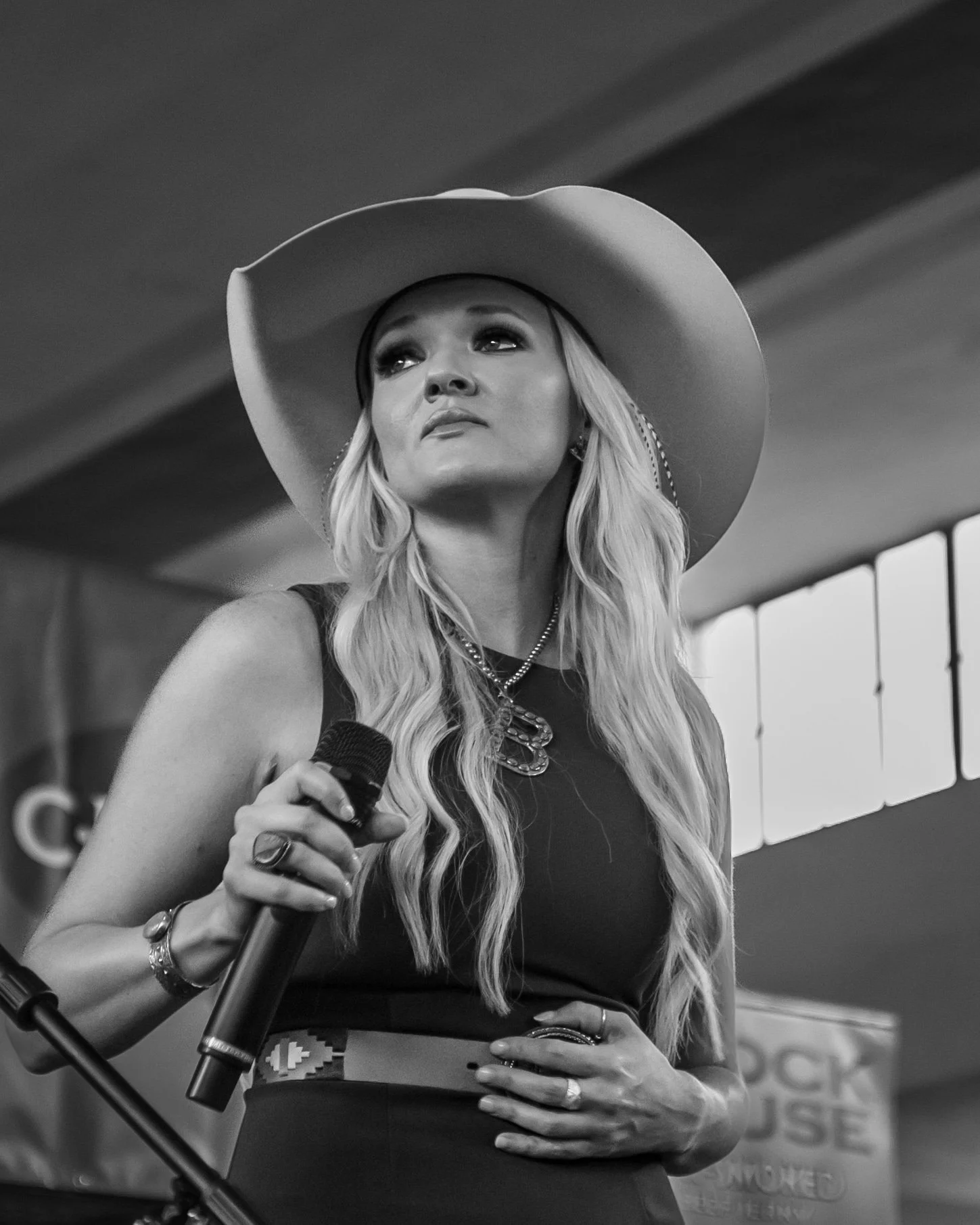 Texas Country musician Billie Jo jones wearing a cowboy hat and holding a microphone, standing indoors with a banner in the background. Concert performance at the Texas State Fair in Dallas Texas in the Go Texan building.
