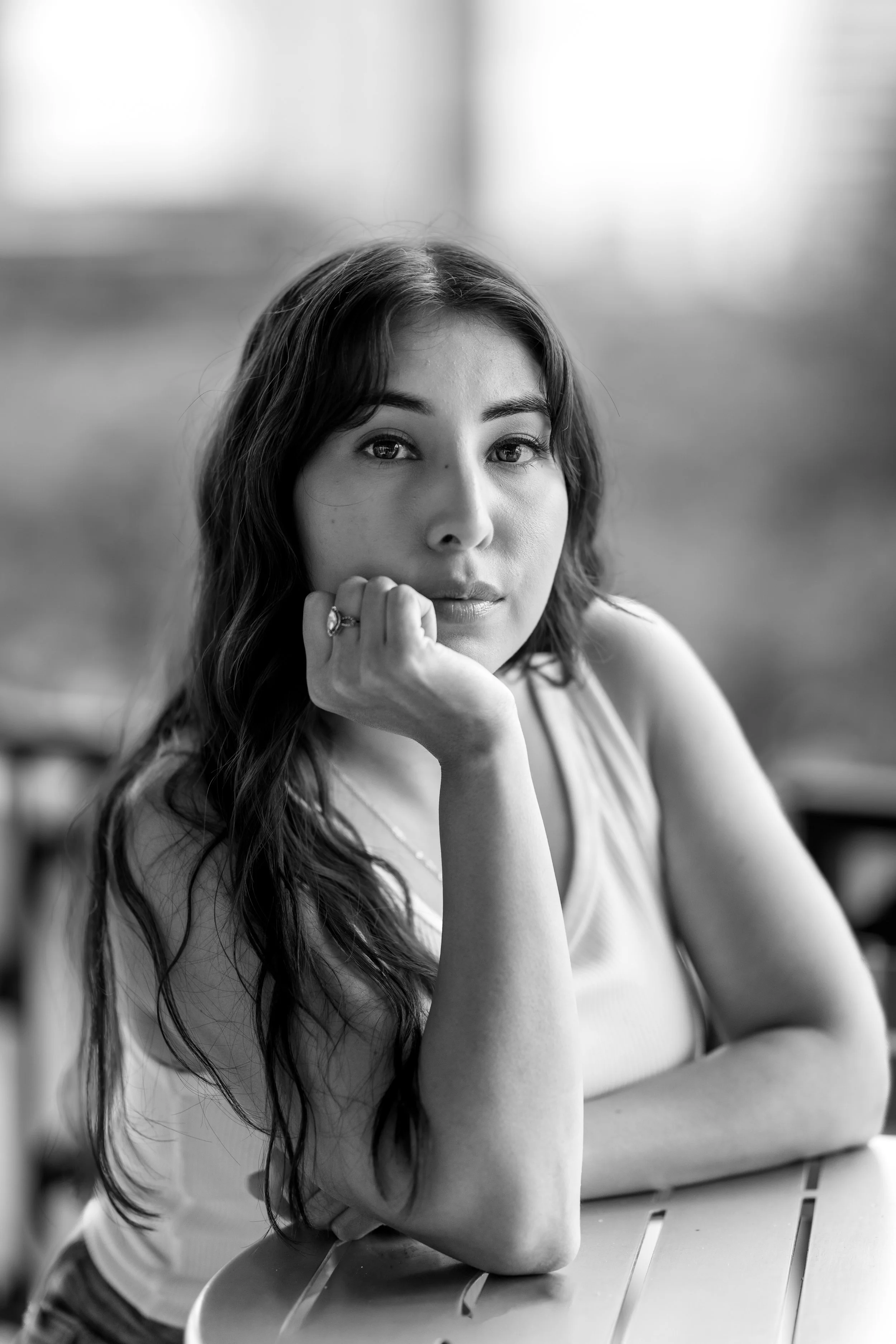 Black and white portrait of a woman looking at the camera while resting head on one hand. Portrait taken in Austin Texas by an Austin Texas photographer.