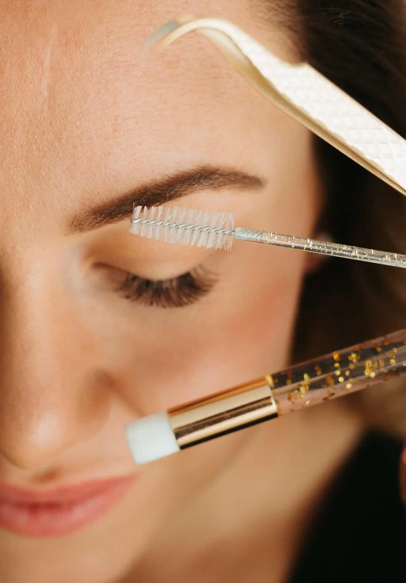 Close-up of a person applying eyelash extension with a tool, focusing on eye and eyebrow.