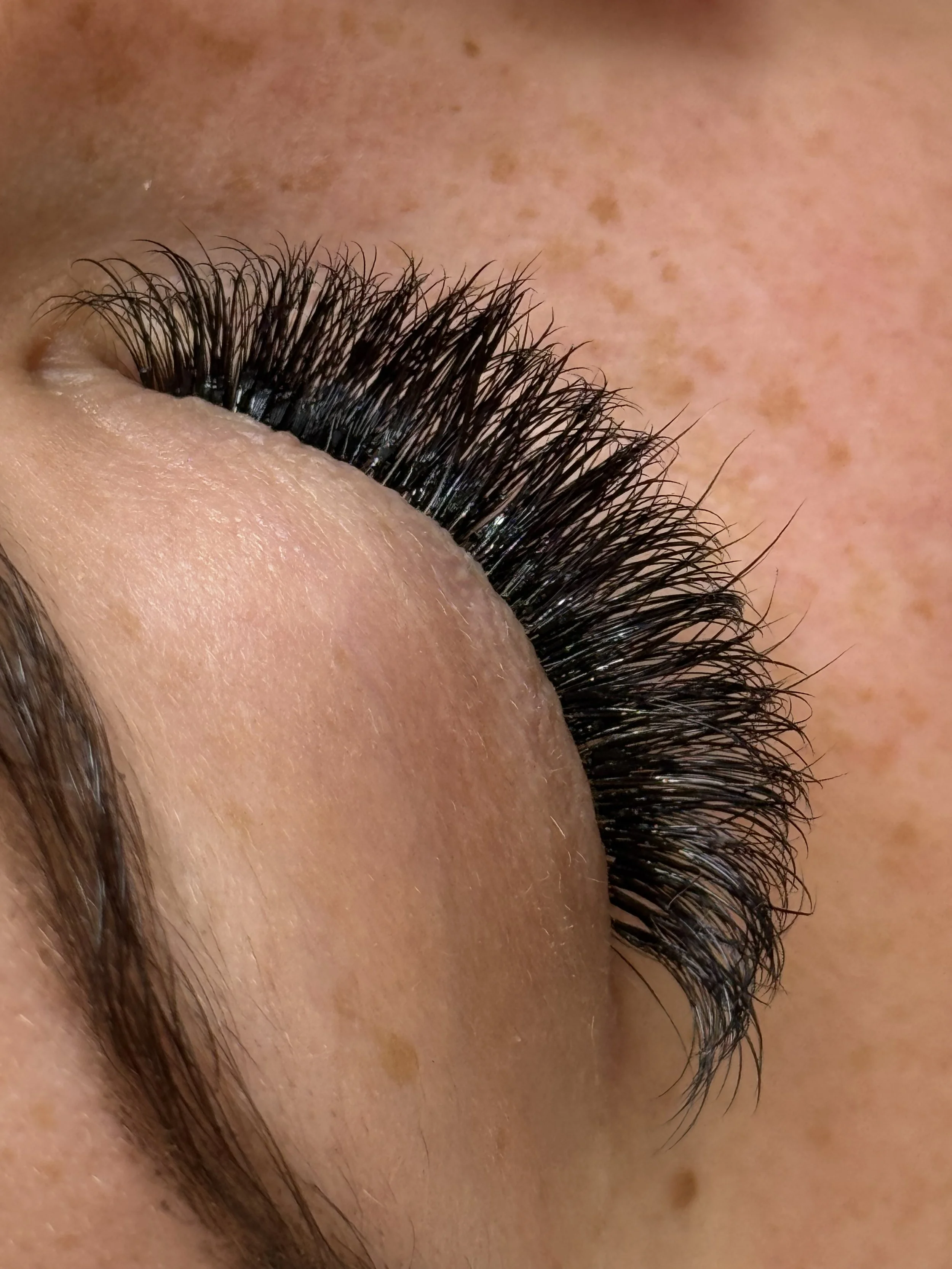 Close-up of a person's closed eye with long, thick eyelashes and freckles on the skin around the eye.