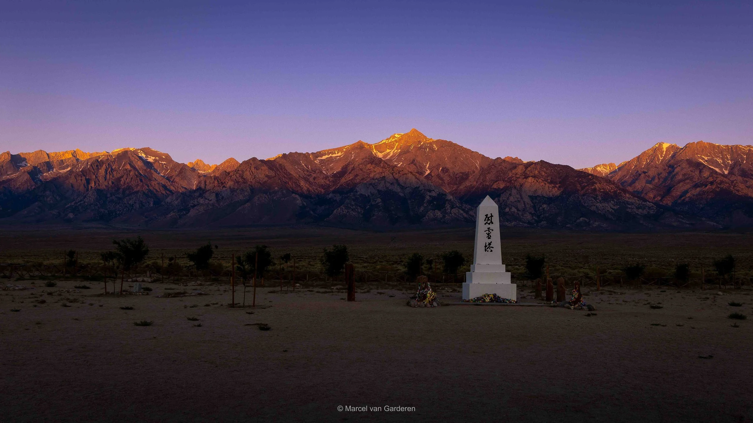 A monument with Japanese characters in a desert landscape with mountains in the background during sunset.