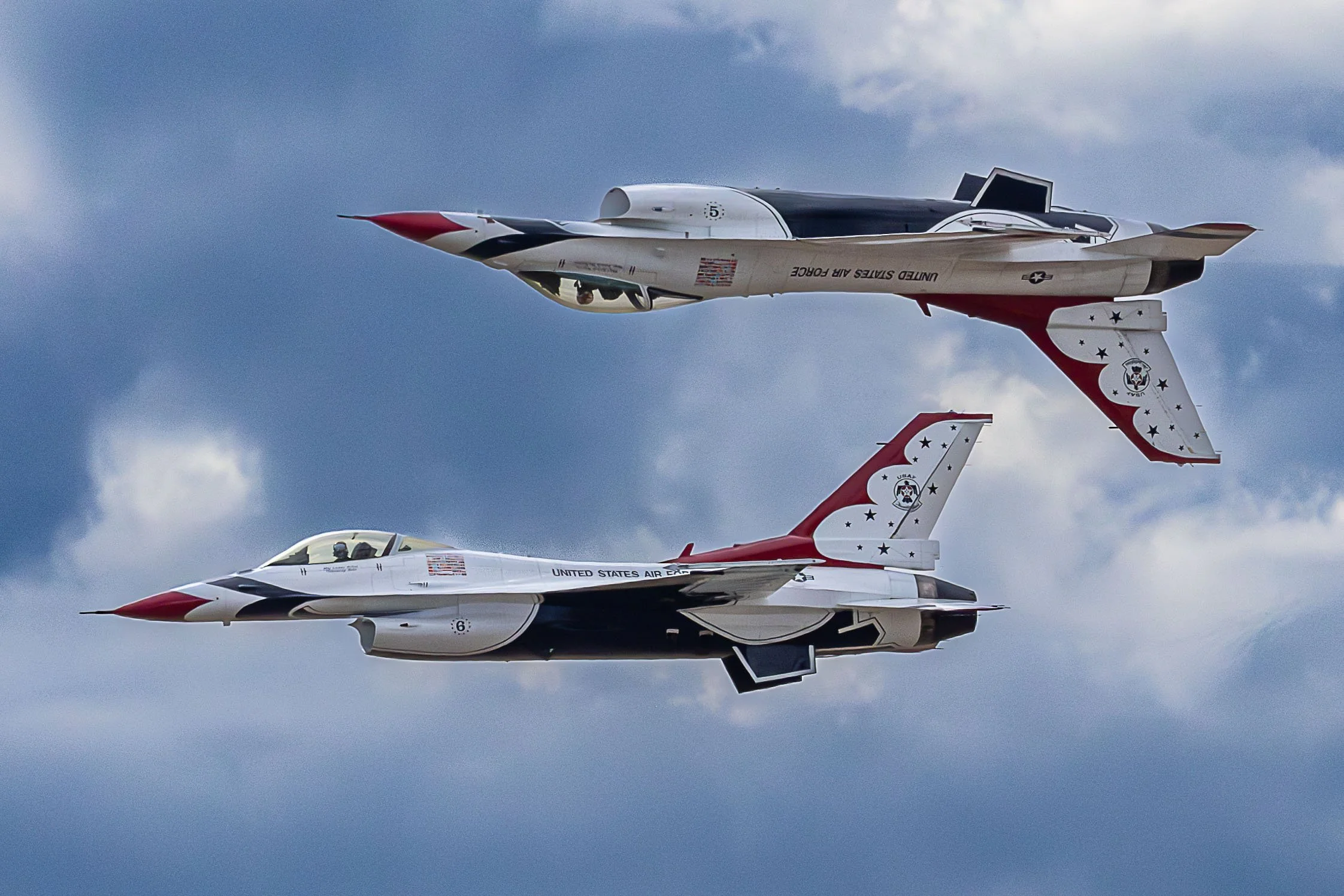 Two United States Air Force F-16 fighter jets flying in close formation against a cloudy sky, with patriotic red, white, and blue paint schemes and insignia.