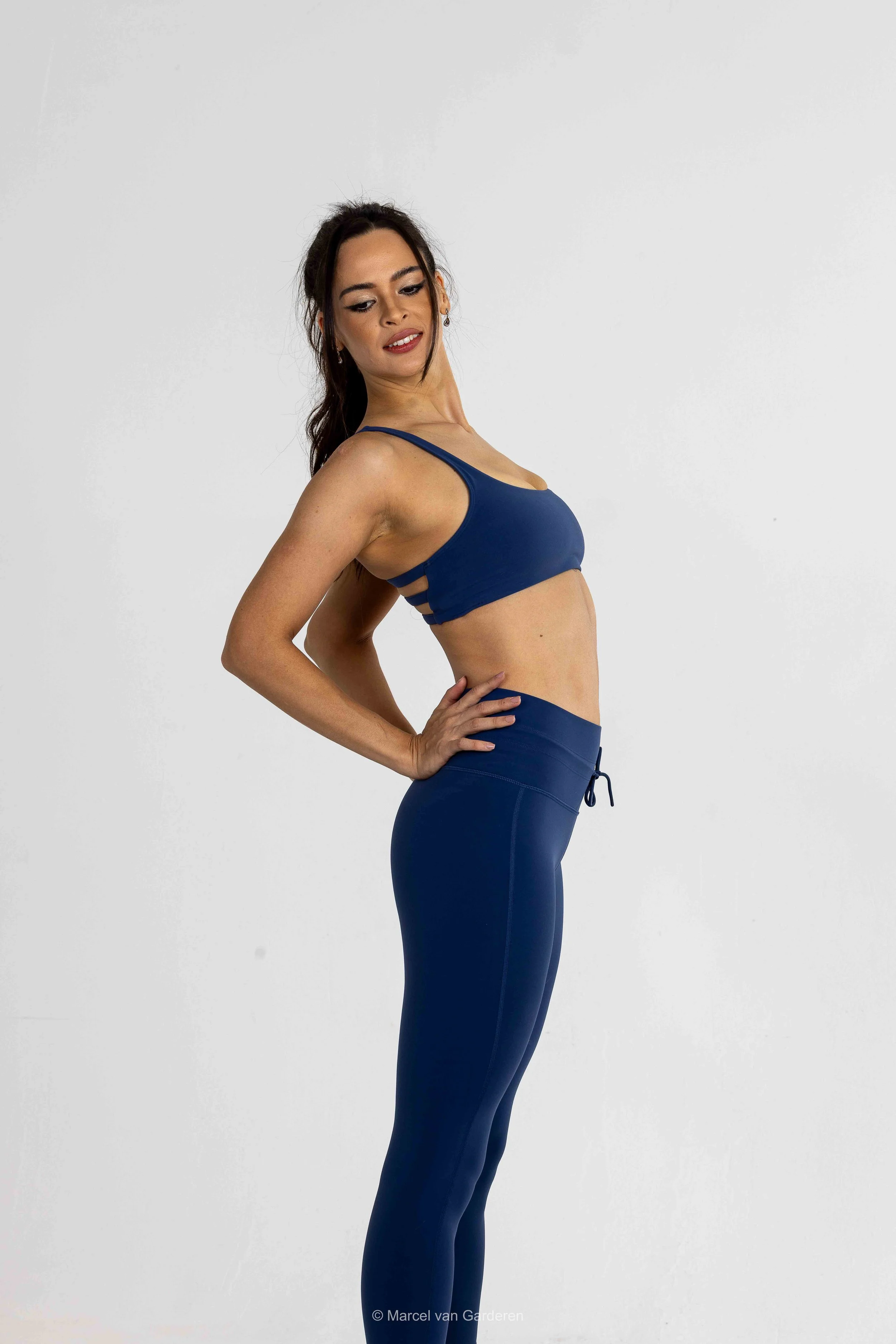 Woman in navy sports bra and matching leggings standing against a plain white background.