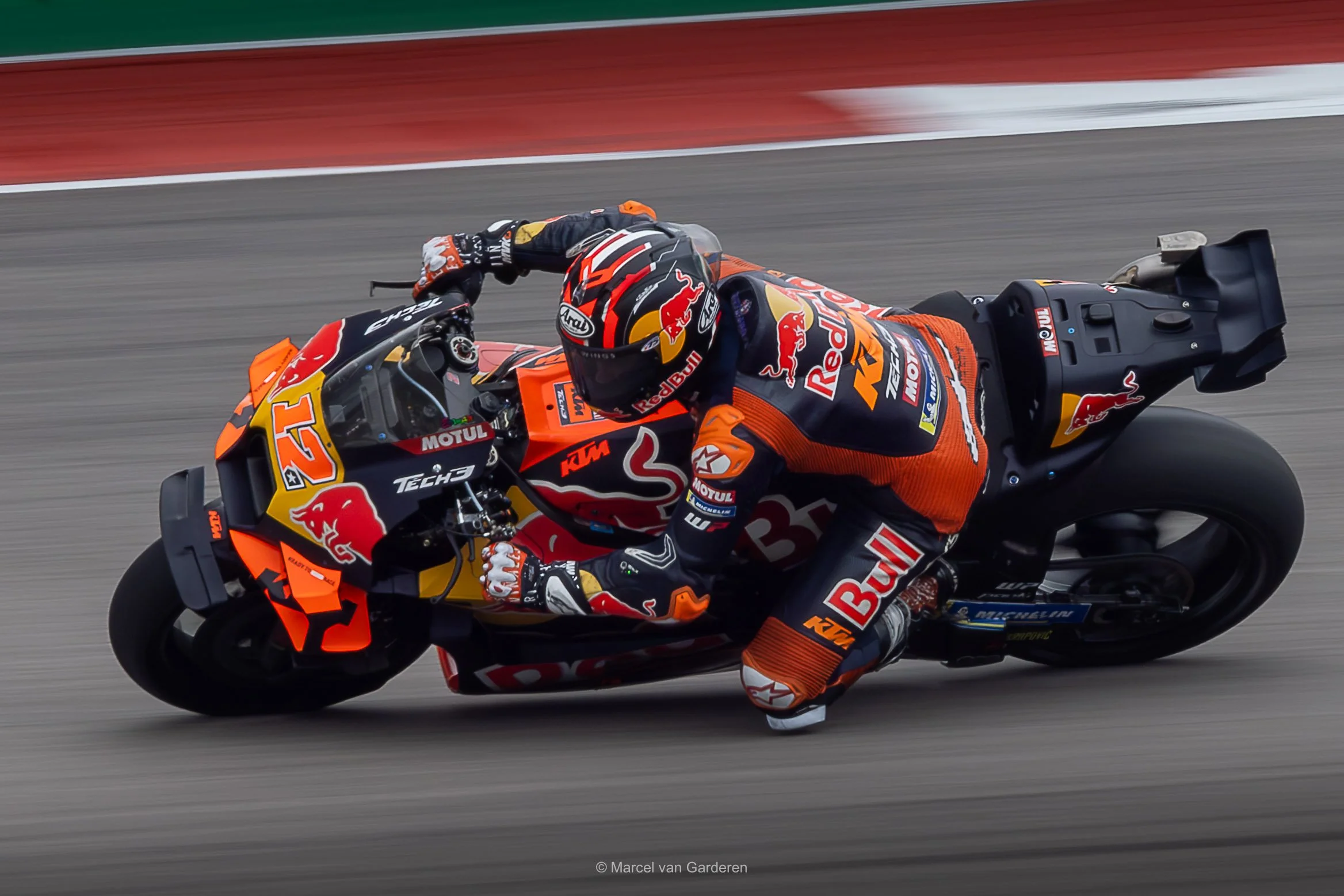 Motorcycle racer in racing gear leaning into a turn on a race track