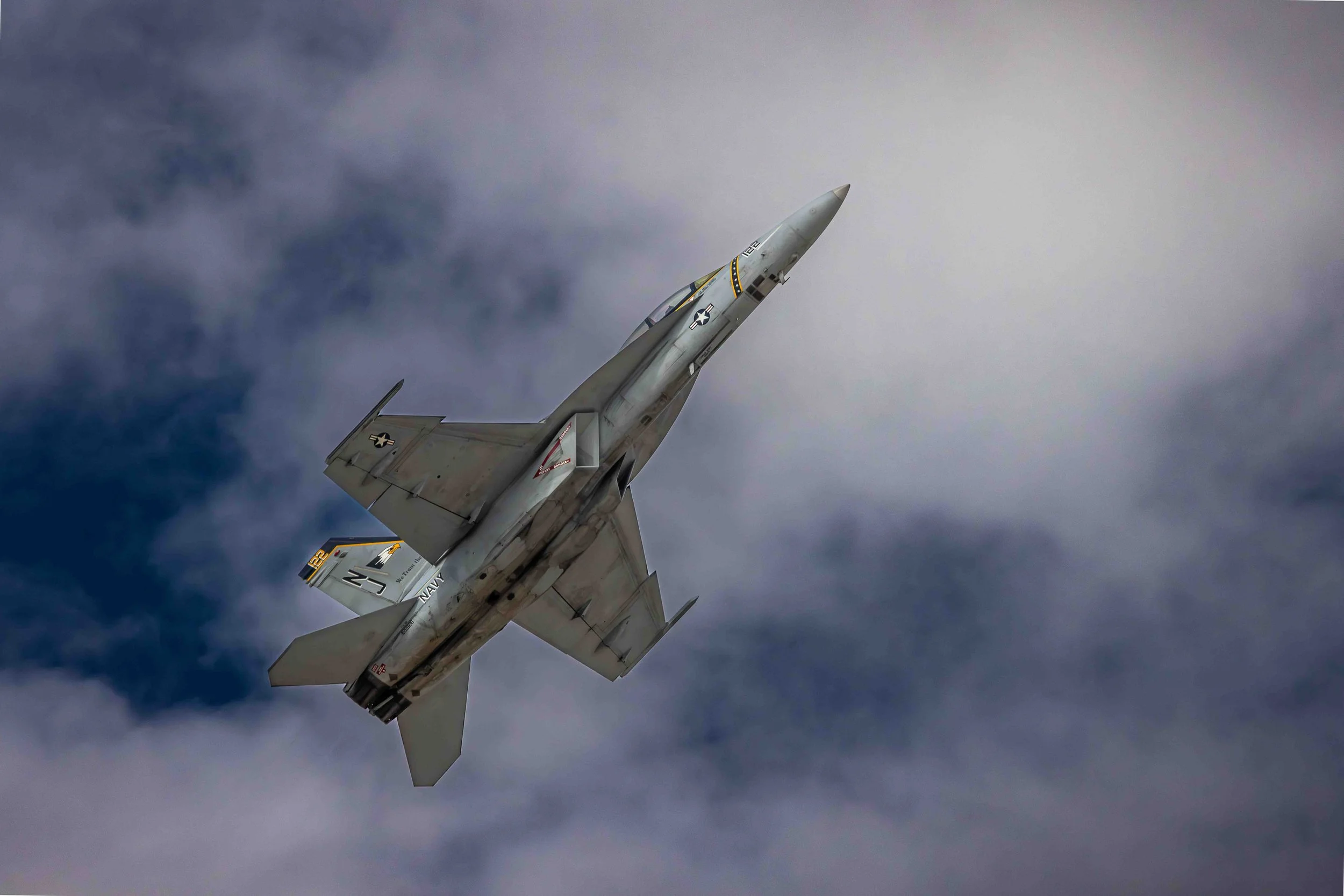 Military fighter jet flying through cloudy sky with gray and white clouds