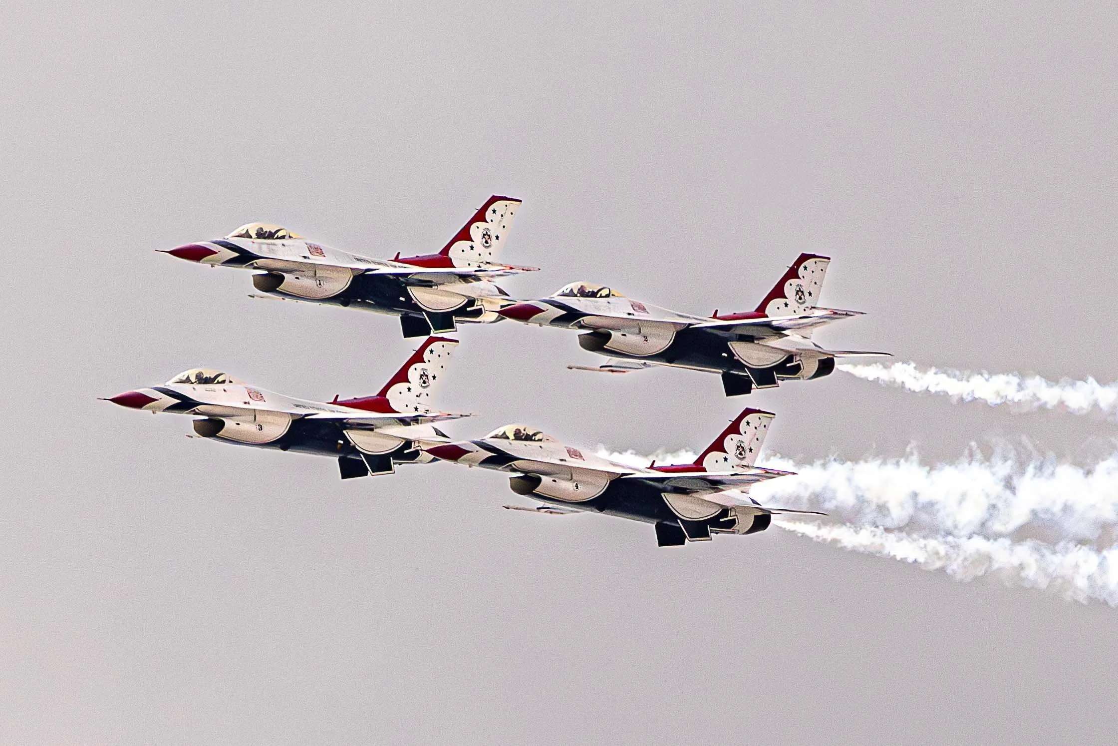 Four fighter jets flying in formation with smoke trails against a gray sky.