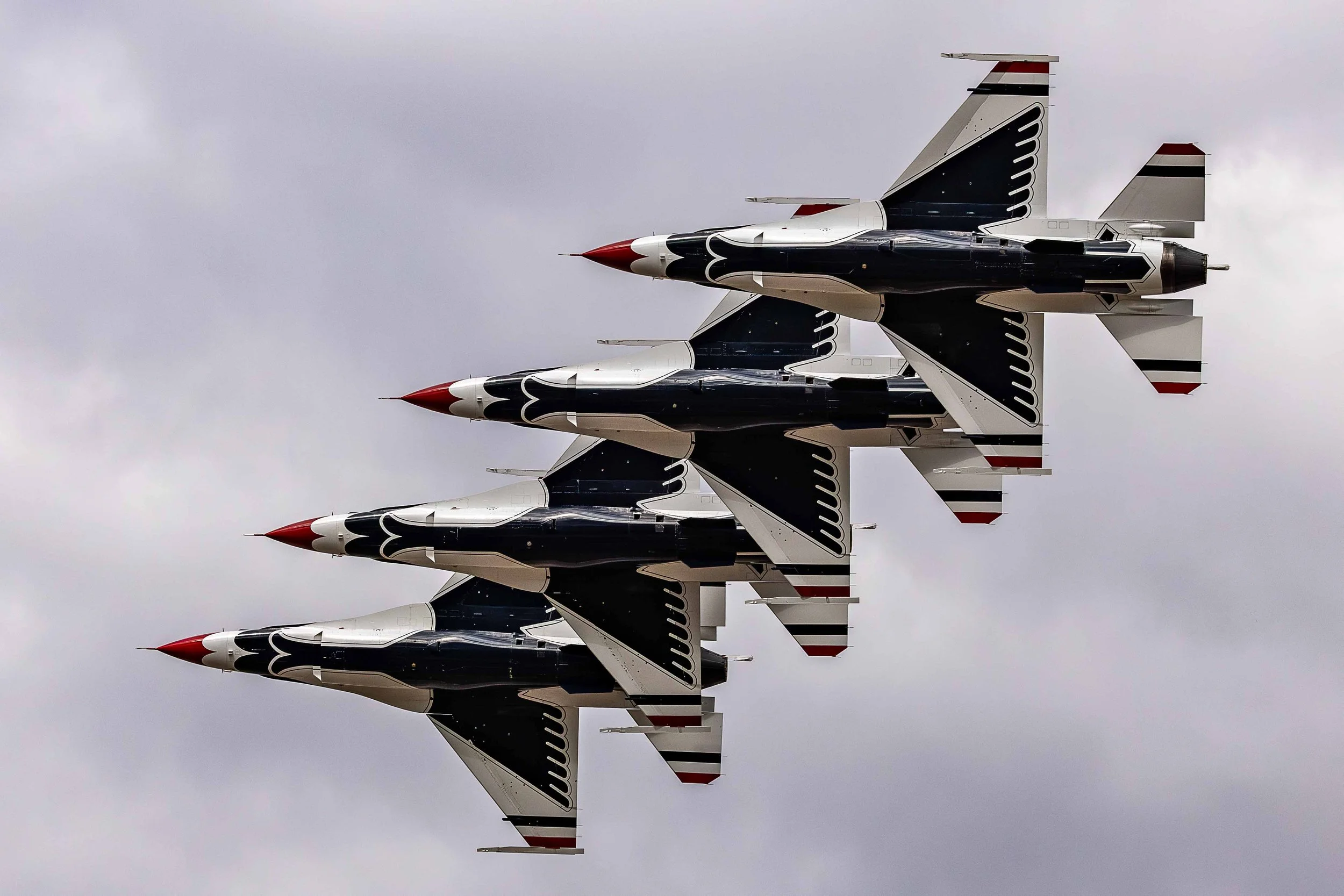 Three fighter jets flying in close formation in a cloudy sky.