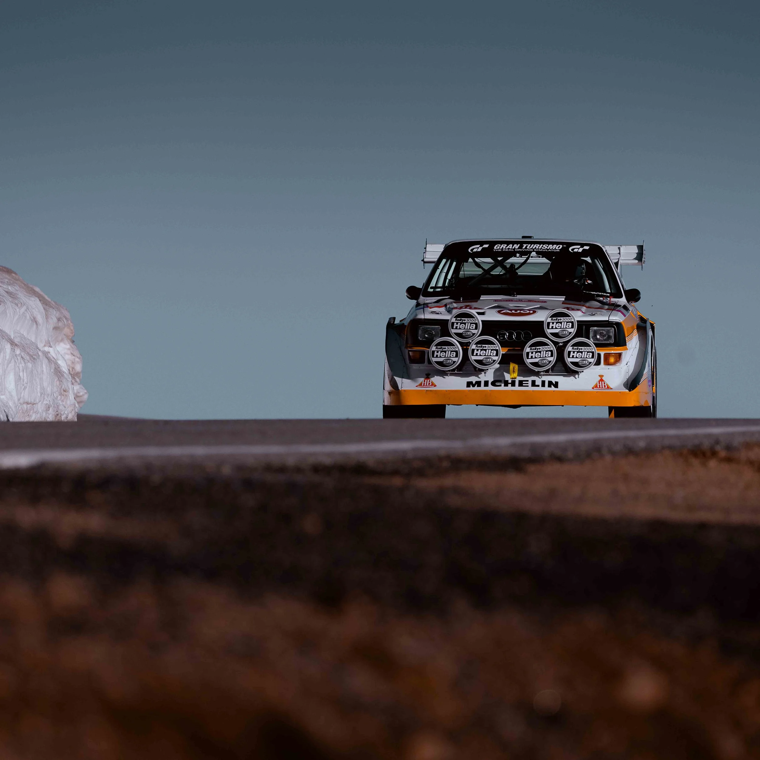A rally car on the road with a rock on the side, viewed from a low angle.