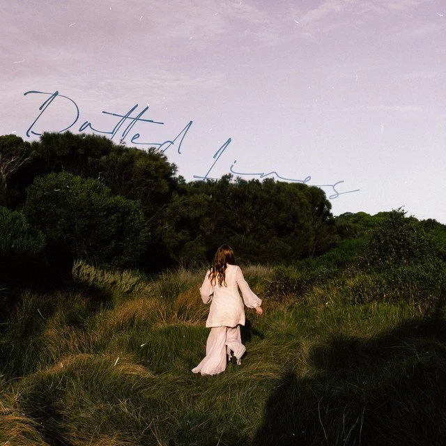 A person in a light pink outfit walking on a grassy trail toward a wooded area at sunset, with the phrase 'Patched Minds' written in cursive across the sky.