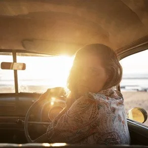 Person sitting in car at sunset with sunlight shining through the window.