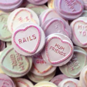 Heart-shaped conversation candies with messages like 'RAILS' and 'MUM FRIENDS' on a pile of similar candies in pastel colors.